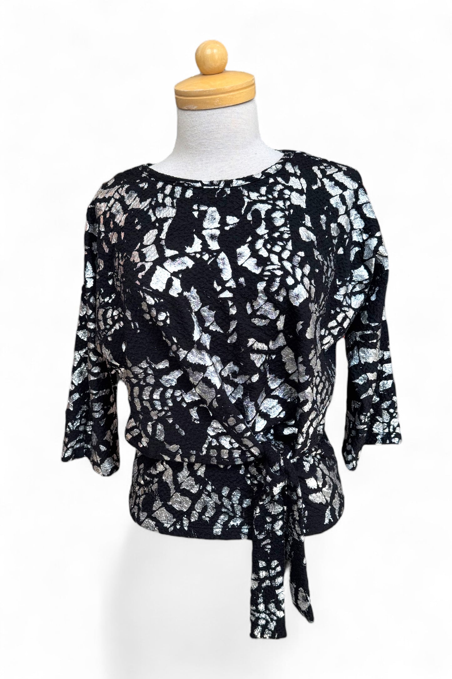 The Posey Sweater from Compli K in Black and Silver, with a round neck, 3/4 sleeves, and a tie detail at the waist, with black pants, is shown on a mannequin in front of a white background.