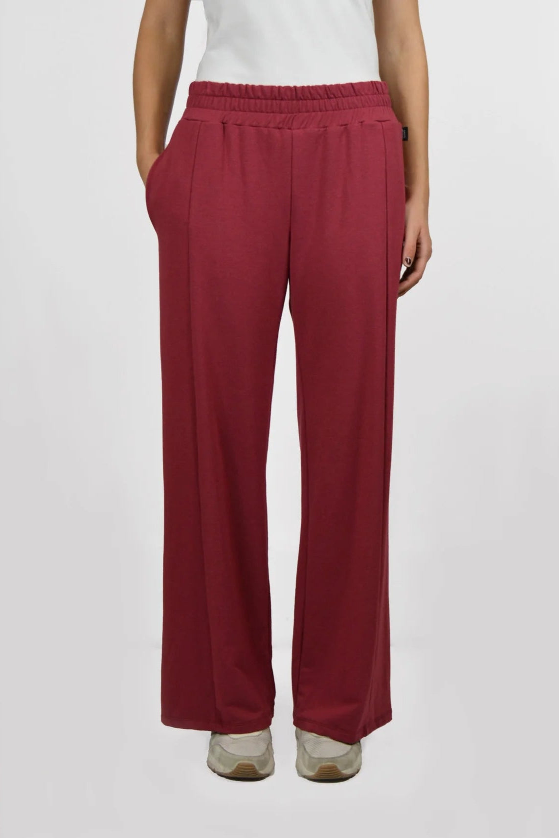 Waist down view of the Tadoussac Pants by Message Factory in Raspberry: flared sweatpants with an elastic waist in a bamboo/cotton blend. She is wearing a white tank with them and is standing in front of a white background.