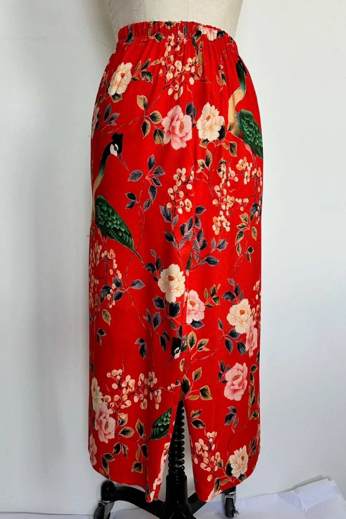 A side view of the Paraiso Pants by Kollontai in Red floral, with an elastic waist, wide cropped legs, and side slits at the hems, is shown on a mannequin in front of a white background.