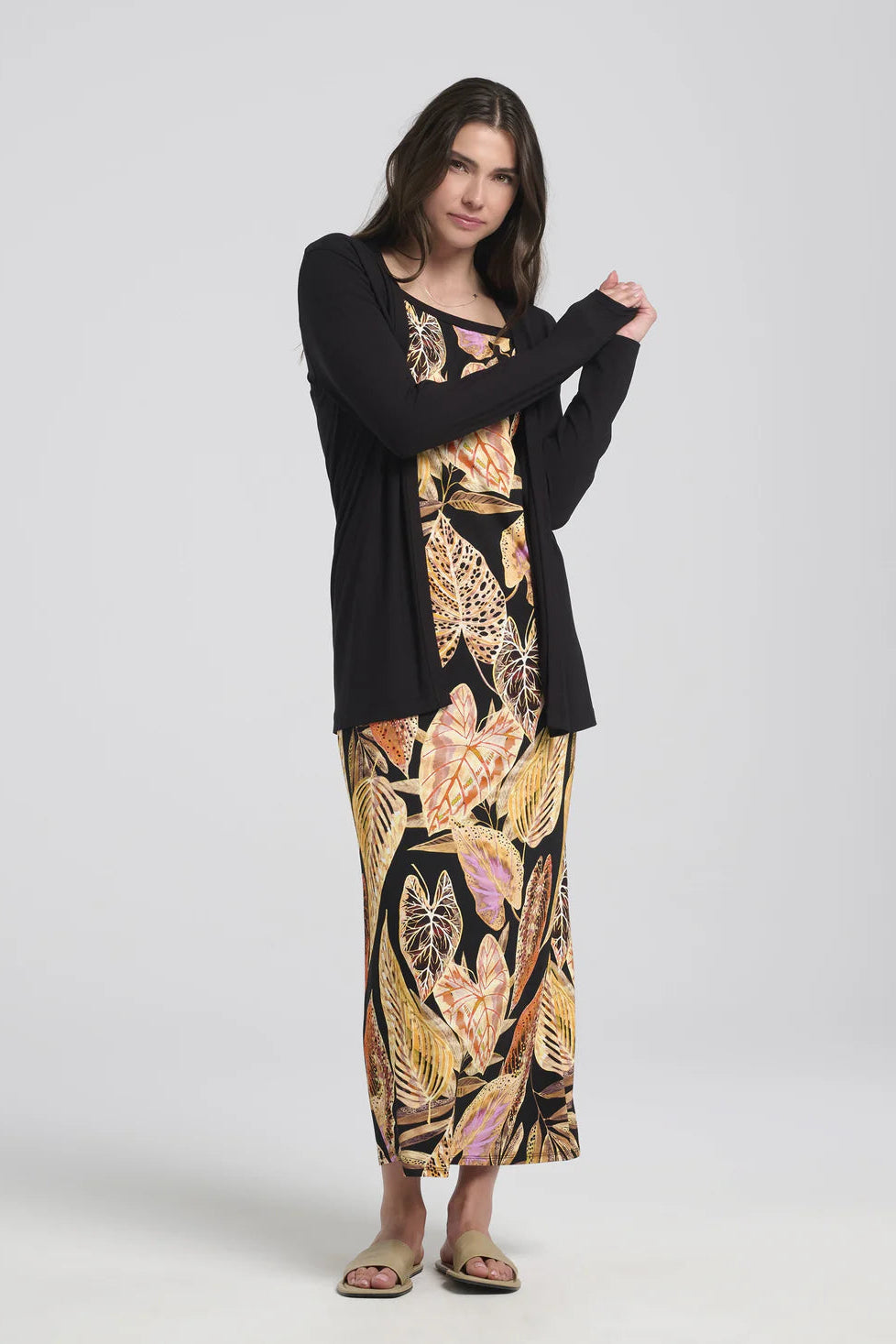 A woman wearing the Umay Cardigan by Kollontai in Black, an open hip-length cardigan made from light viscose. She is wearing it over a print dress and is standing in front of a white background.