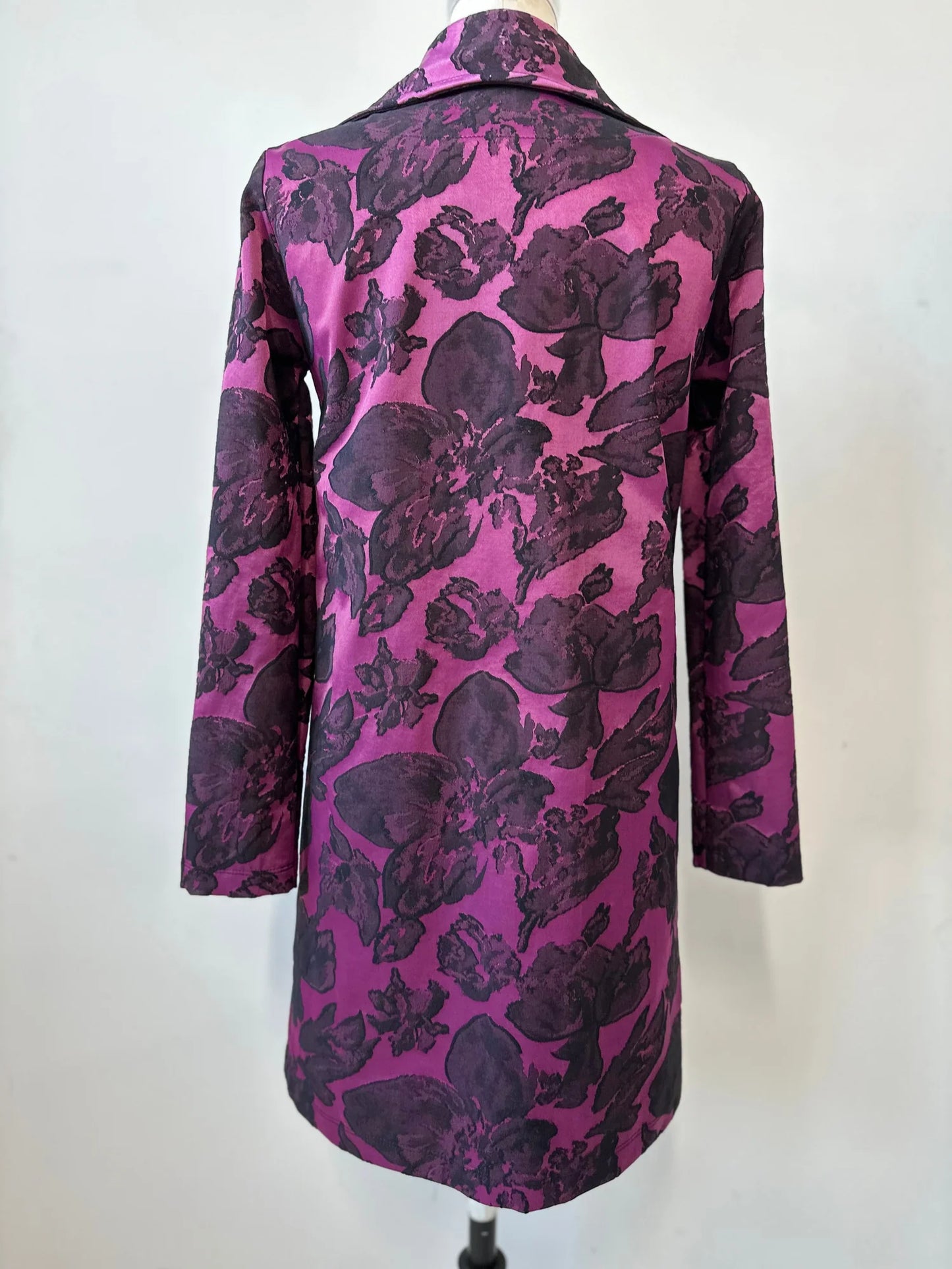 Back view of the Amarante Coat by Kollontai in Blackberry shown on a mannequin against a white background. It's a satin coat with an intricate floral pattern, a classic collar, button front, straight cut that hits above the knee, and large pockets.