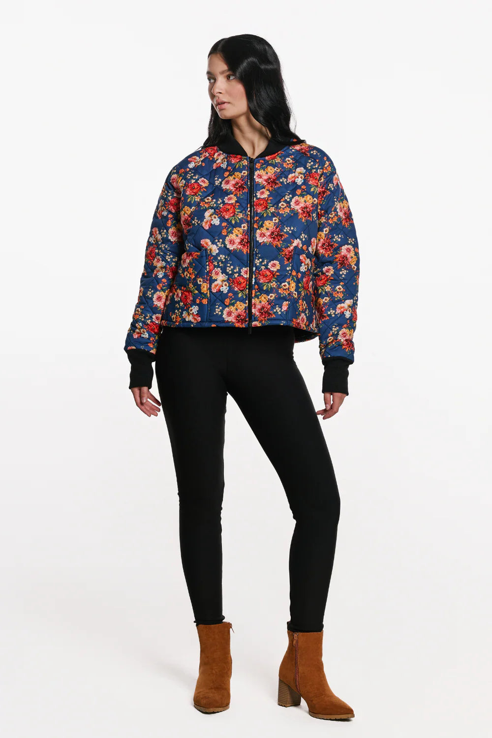A woman wearing the Harper Bomber Jacket by EMK, a floral bomber jacket in quilted fabric with black waffle knit fabric at the cuffs and collar. She is wearing it with black pants and standing in front of a white background.
