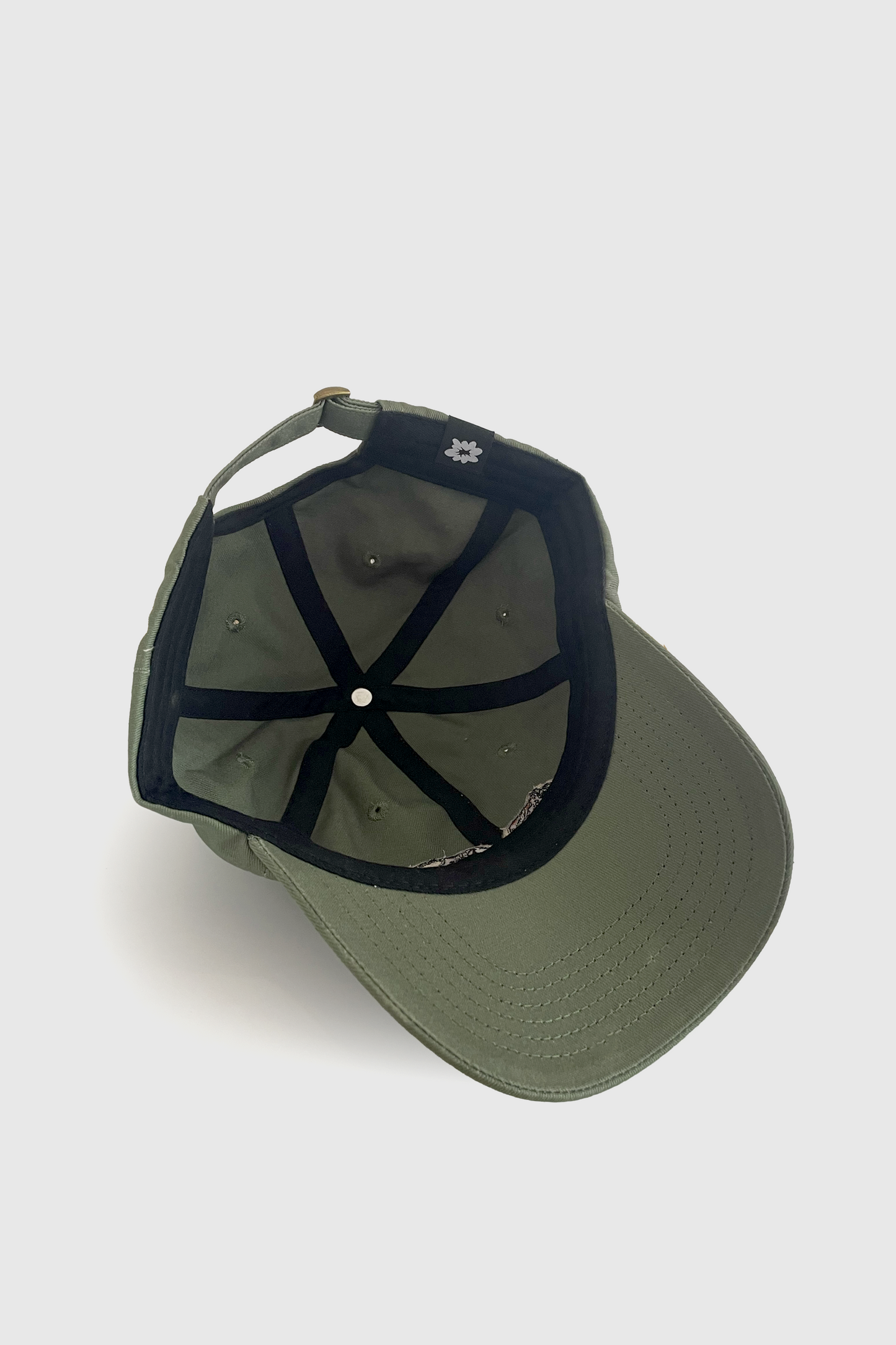 Inside view of the Hop Hat by Badaboöm Studio, a sage green baseball cap featuring embroidered split tiger graphic on the front, set against a light grey background.