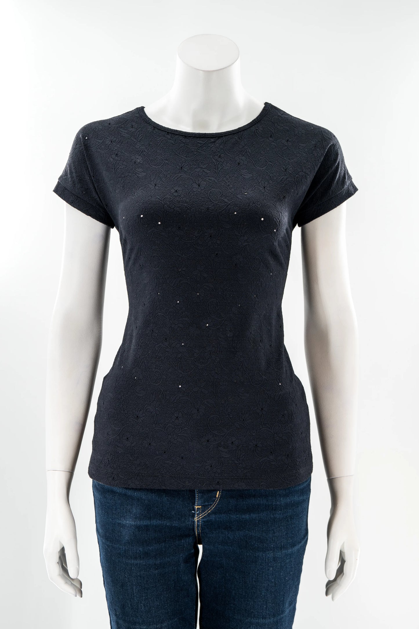 The Tourmaline T-Shirt by Karkass in Black, featuring a subtle floral texture with tiny cut-outs, is show on a mannequin in front of a white background.