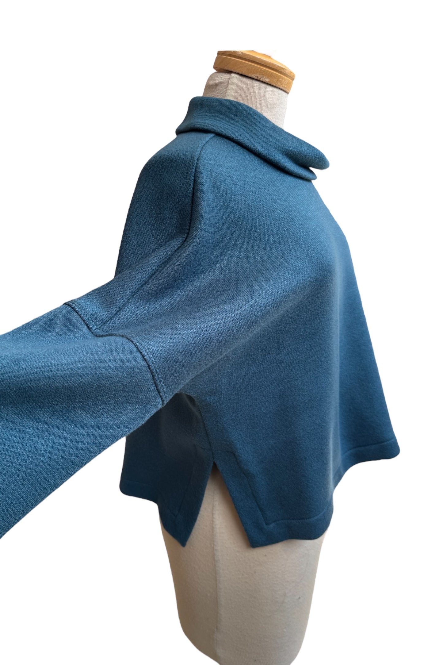 A side view of the Paige Sweater by Compli K in Peacock, featuring a large cowl neck, drop-sleeves, a loose fit, and side slits, is shown on a mannequin against a white background.
