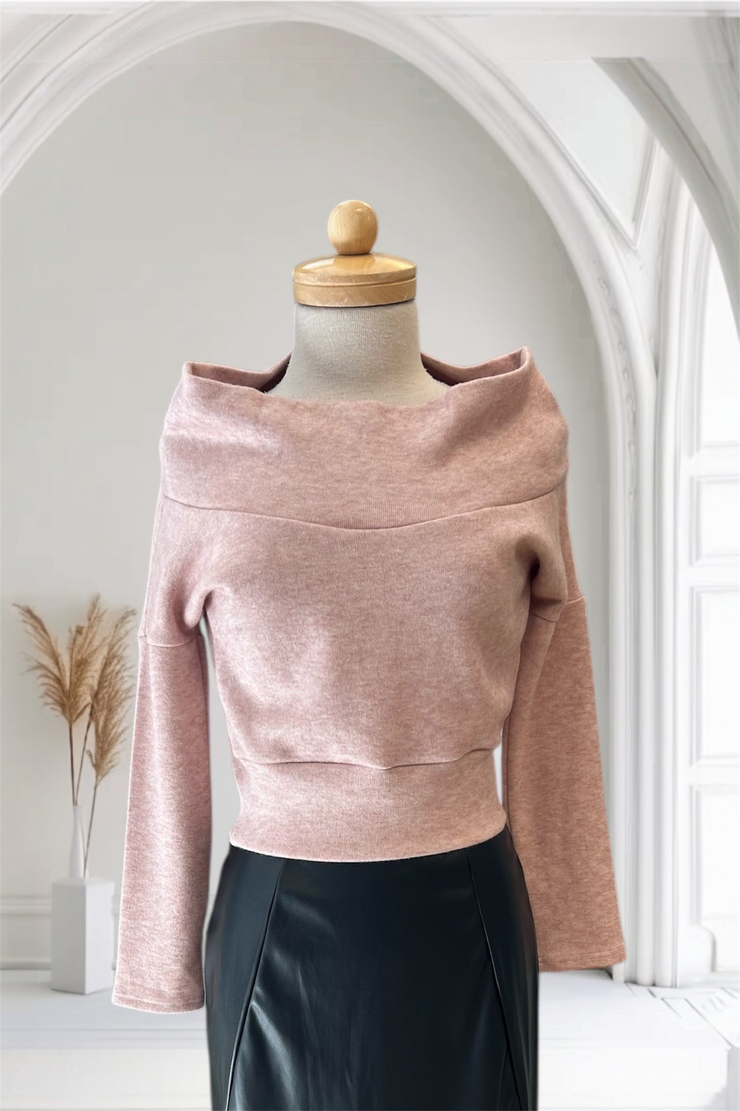 The Changes Sweater by Allison Wonderland in Pink, featuring a large cowl neck, long dropped sleeves, and a wide waistband, is shown with the Desire Skirt in Black against a white arched backdrop.