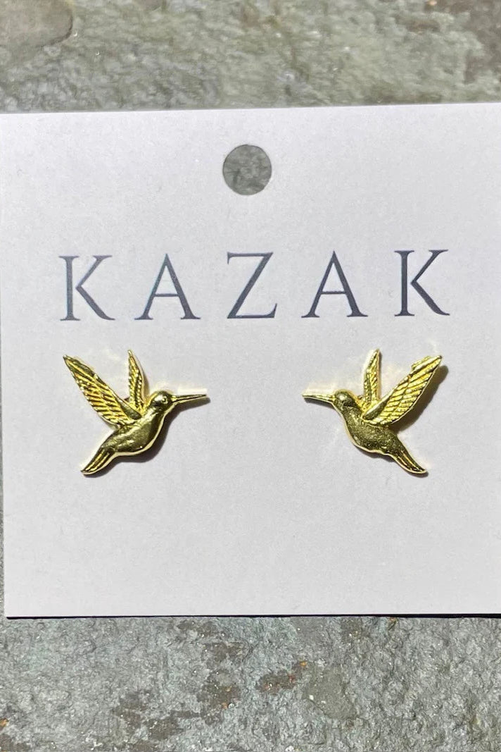 Brass hummingbird earrings on a 'KAZAK' branded card against a textured grey background