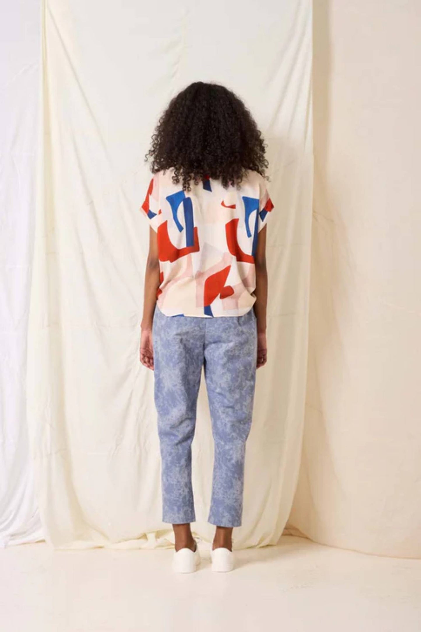 Back view of a woman wearing the Ombre Top by Cokluch in Vera print, standing in front of a white curtain