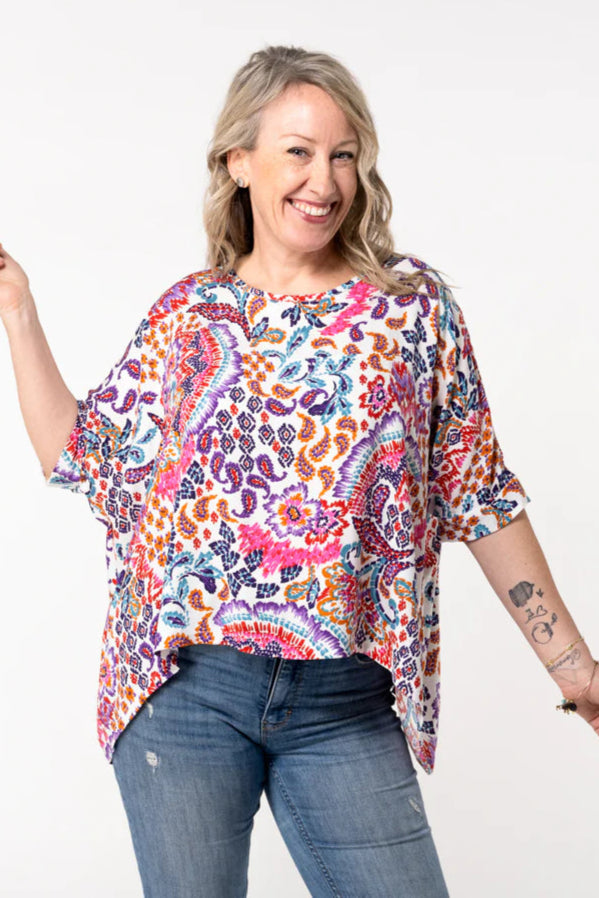 A woman wearing the Chloe Top by Desserts and Skirts in Paisley, featuring a round neck, batwing sleeves, and a loose and flowing fit. She is wearing it with jeans and is standing in front of a white background.