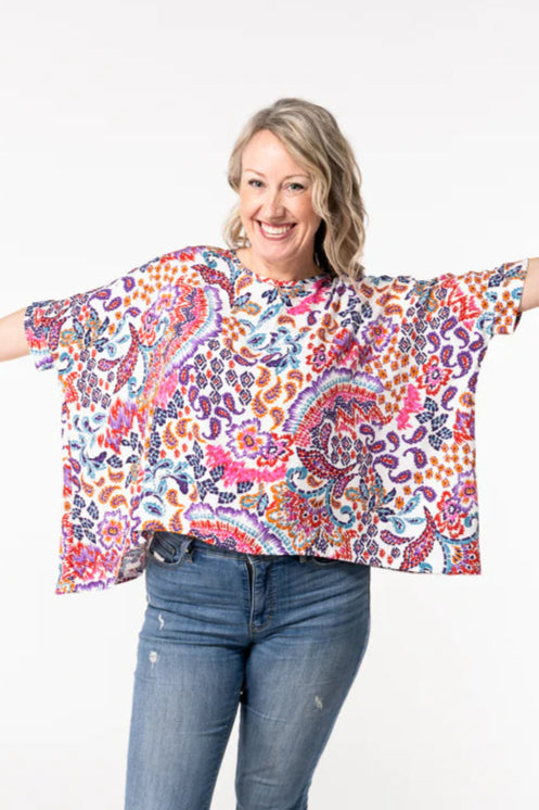 A woman wearing the Chloe Top by Desserts and Skirts in Paisley, featuring a round neck, batwing sleeves, and a loose and flowing fit. She is wearing it with jeans and is standing in front of a white background.