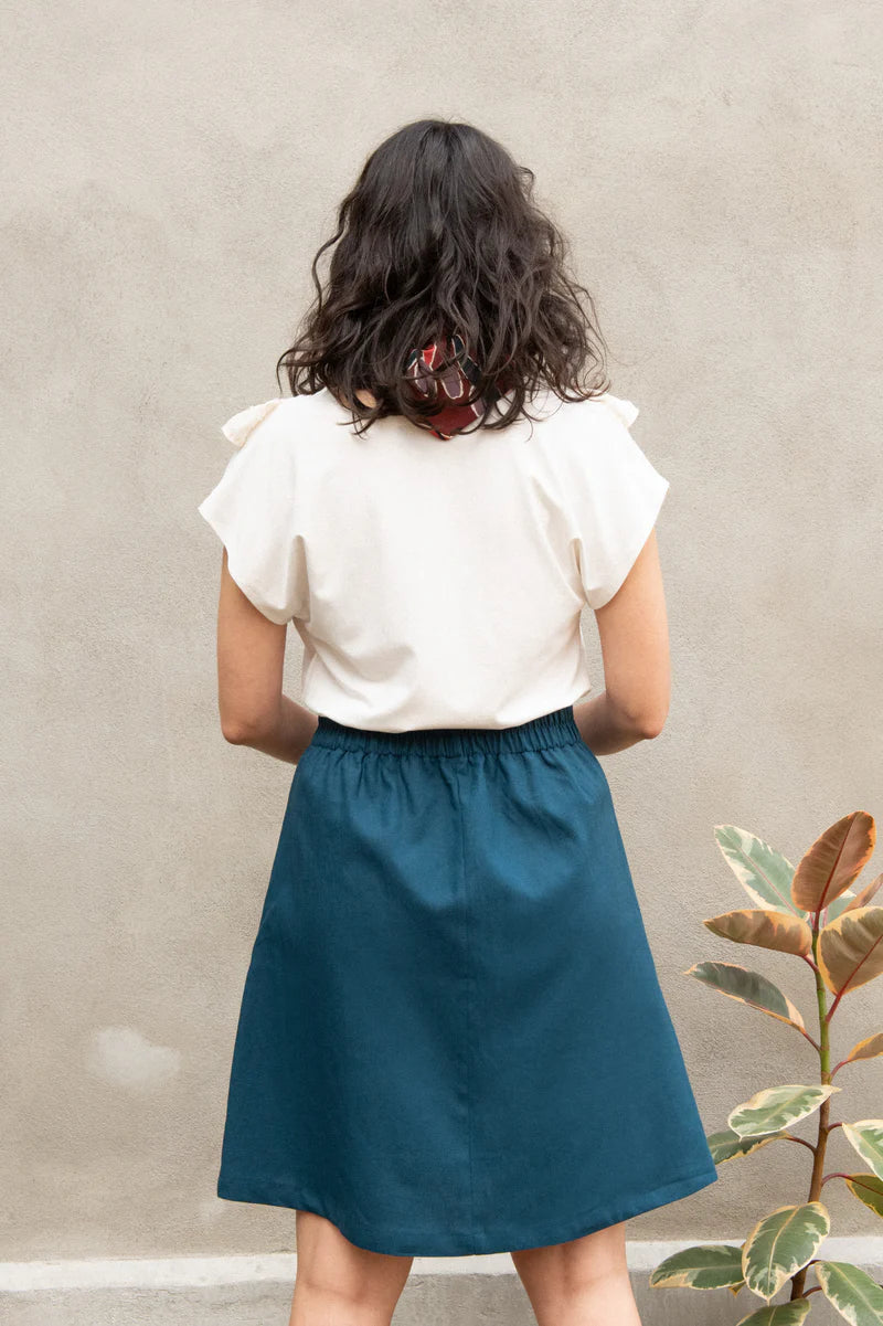 Chrysanthème Skirt by Kazak, Teal, back view, knee-length, A-line, elastic at sides and back of waist, brass buttons up the front, two large pockets, eco-fabric, linen, rayon, sizes XS to XL, made in Montreal 