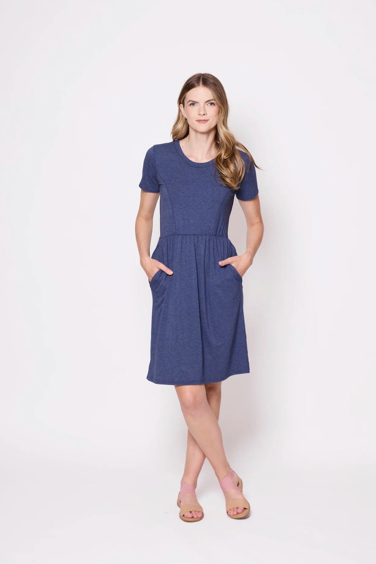 A woman wearing the Hayley Dress by Tangente in Heather Lake, a short sleeved bamboo dress with a gathered knee-length skirt. She is standing outside in front of a white background.