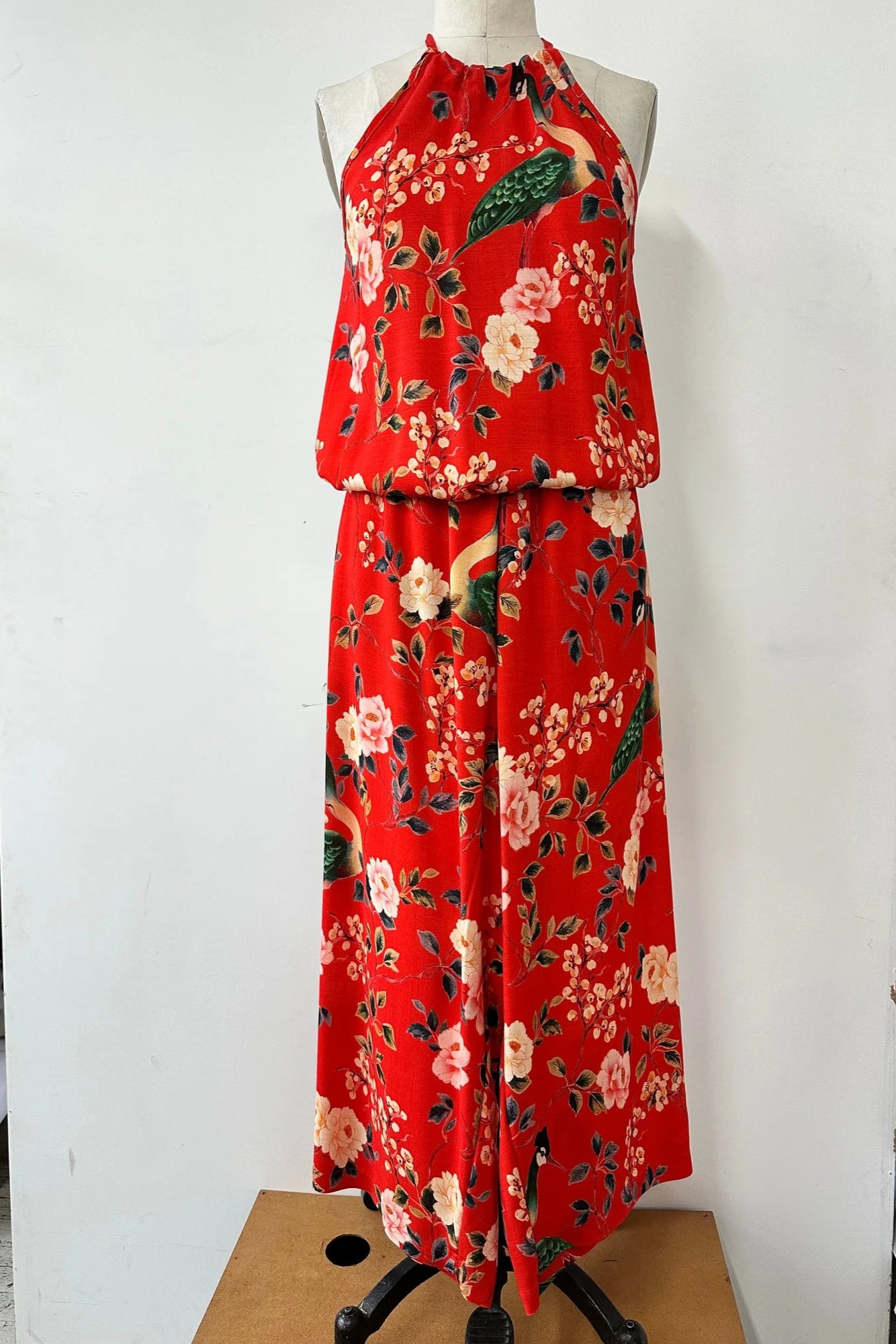 The Zephyrine Jumpsuit by Kollontain Red floral, with a halter neck, elastic waist with a bloused effect, and wide cropped legs, is show on a mannequin in front of a white background.