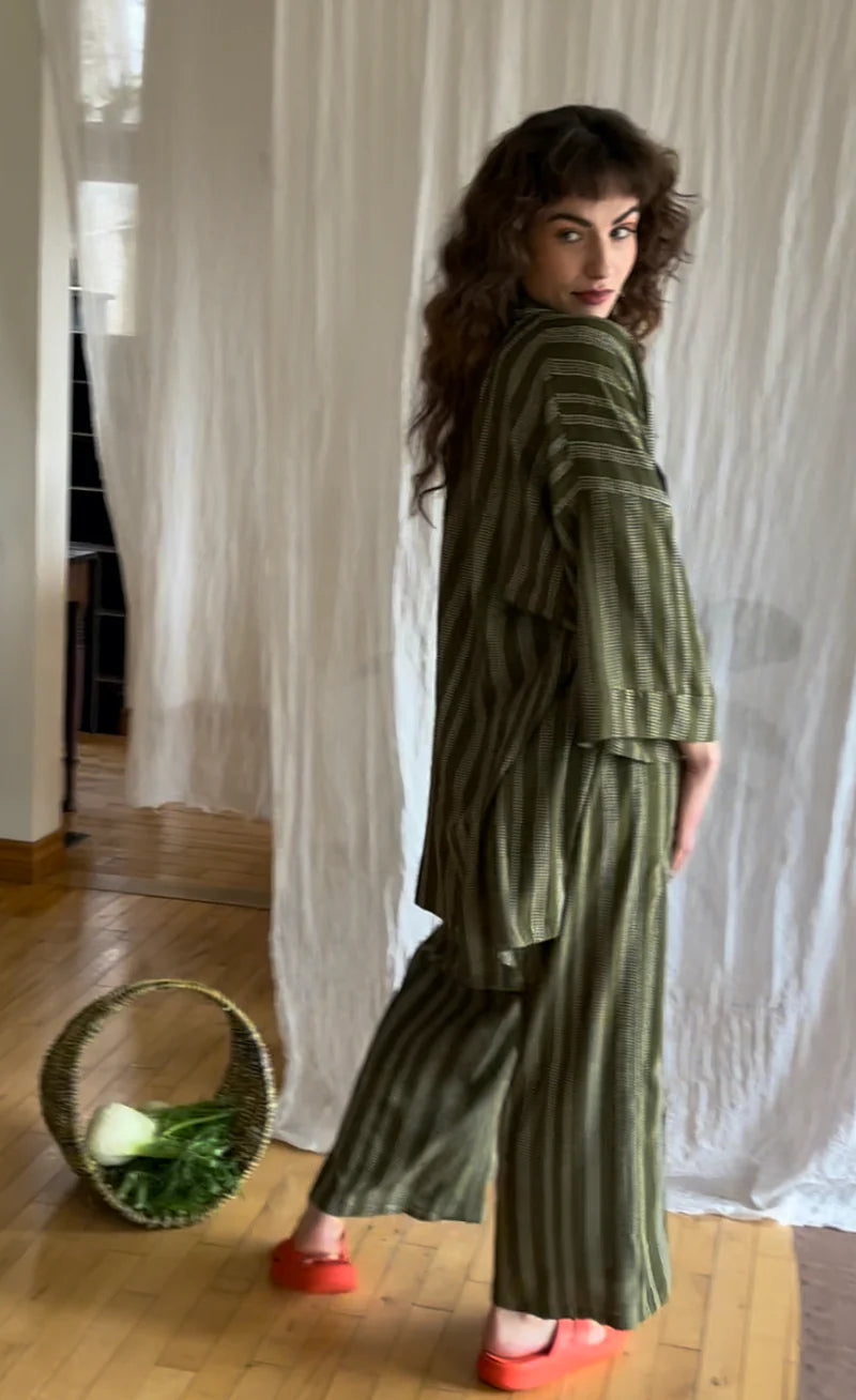 Side view of a woman wearing the Mirano Jacket by Kazak in Ivy Dots print, an open Kimono-inspired jacket that falls to mid-thigh and has wide 3/4 sleeves. She is wearing it with the matching Sienna Pants and is standing in front of a white curtain.