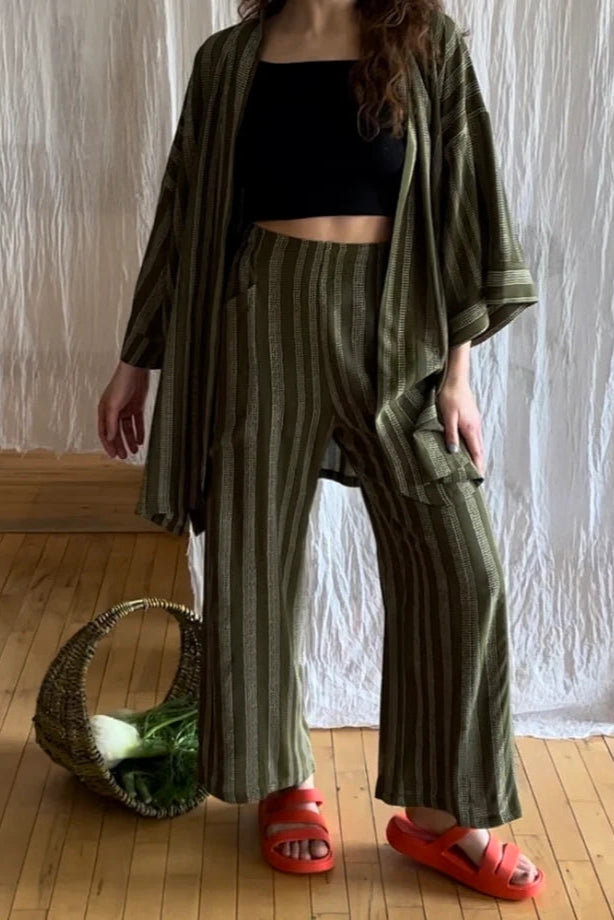 A woman wearing the Mirano Jacket by Kazak in Ivy Dots print, an open Kimono-inspired jacket that falls to mid-thigh and has wide 3/4 sleeves. She is wearing it with the matching Sienna Pants and is standing in front of a white curtain.