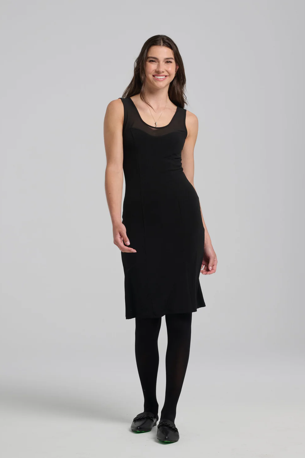 A woman wearing the Shelley Dress by Kollontai in Black, with black tights, standing in front of a white background