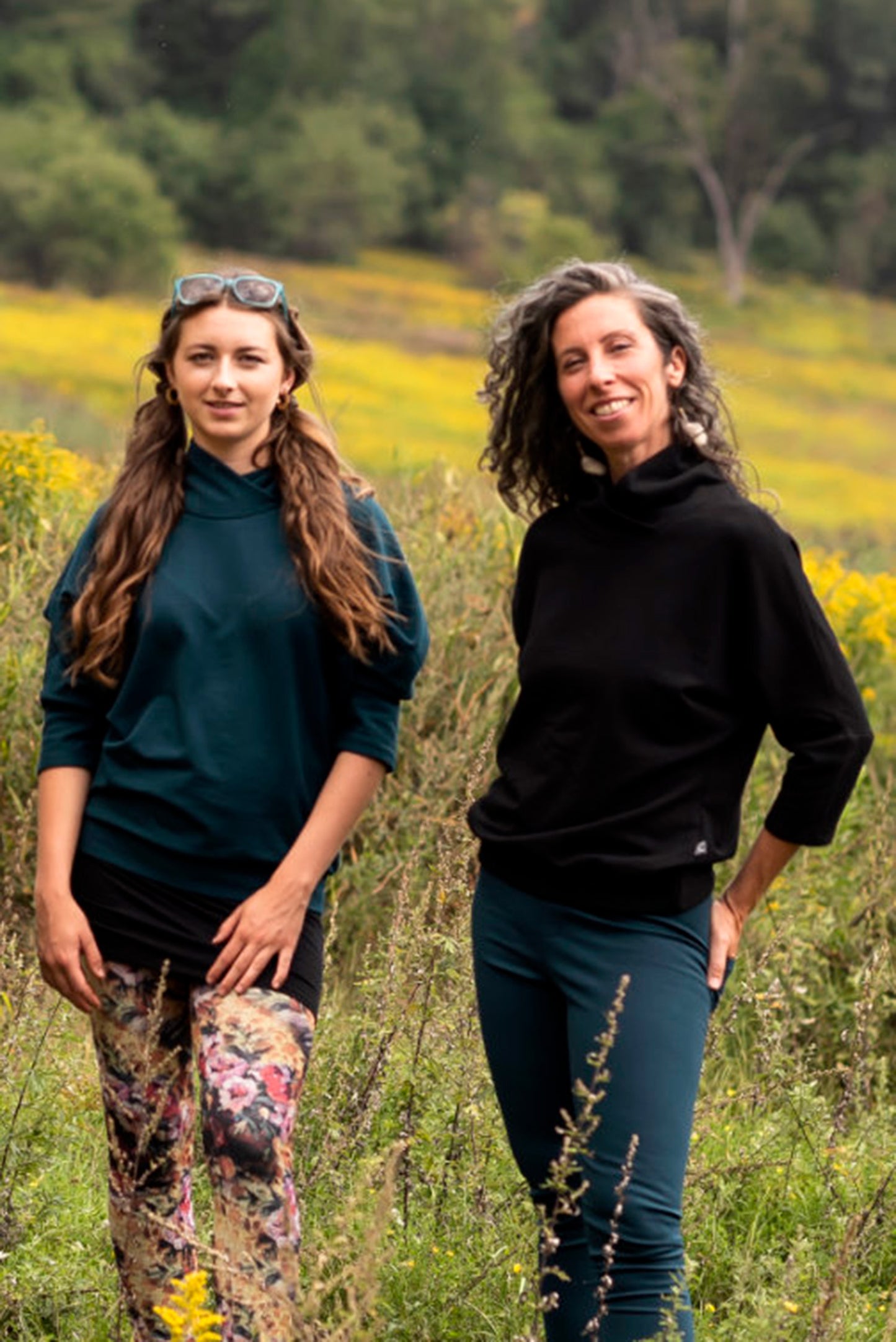 A woman wearing the Beaaa Top by Marie C in Everglade, and a woman wearing the Beaaa Top by Marie C in Black, standing in a field
