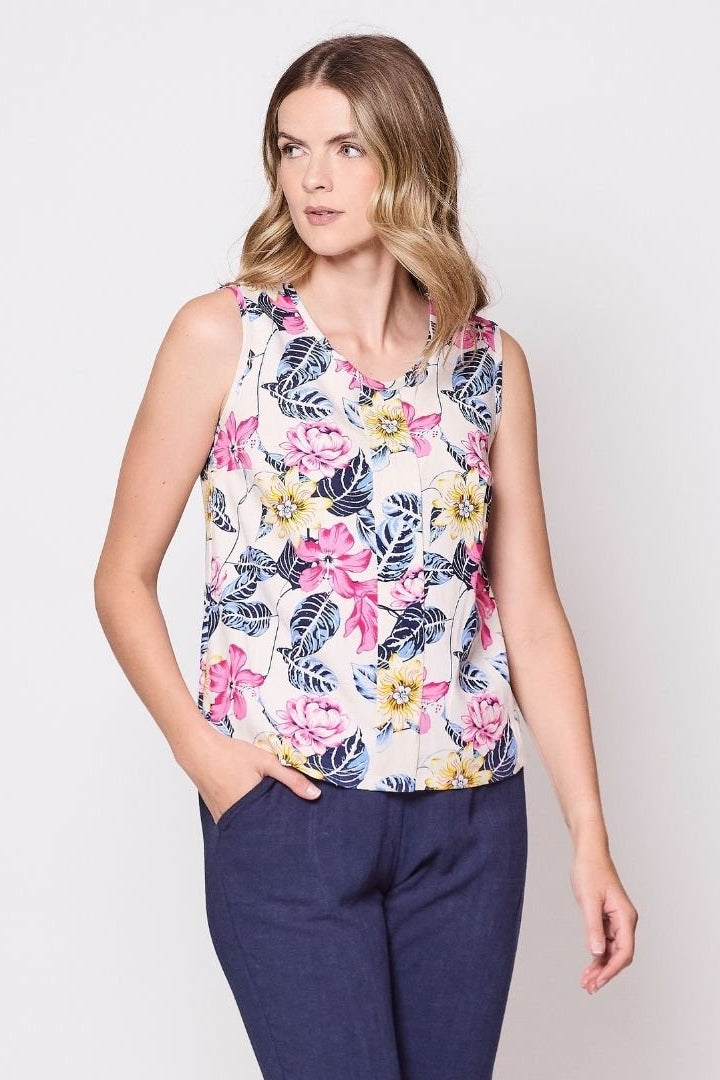 3/4 view of a woman wearing the Marney Tank Top by Tangente in White Floral, with a round neck, full-length centre pleat, and darts at the bust. She is wearing it with navy pants and standing in front of a white background.