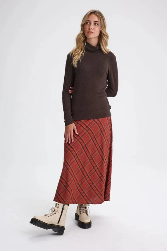 A woman wearing the Gatineau Turtleneck by Message Factory in Brown, a classic turtleneck in a bamboo and cotton blend, with an orange plaid shirt. She's standing in front of a white background.