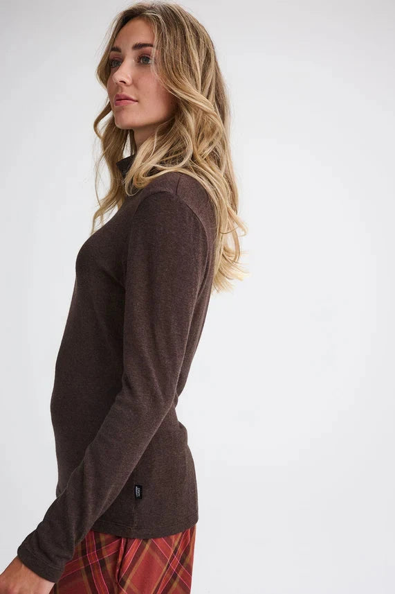 Side view of a woman wearing the Gatineau Turtleneck by Message Factory in Brown, a classic turtleneck in a bamboo and cotton blend, with an orange plaid shirt. She's standing in front of a white background.