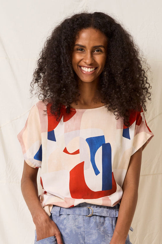 A woman wearing the Ombre Top by Cokluch in Vera print, standing in front of a white curtain