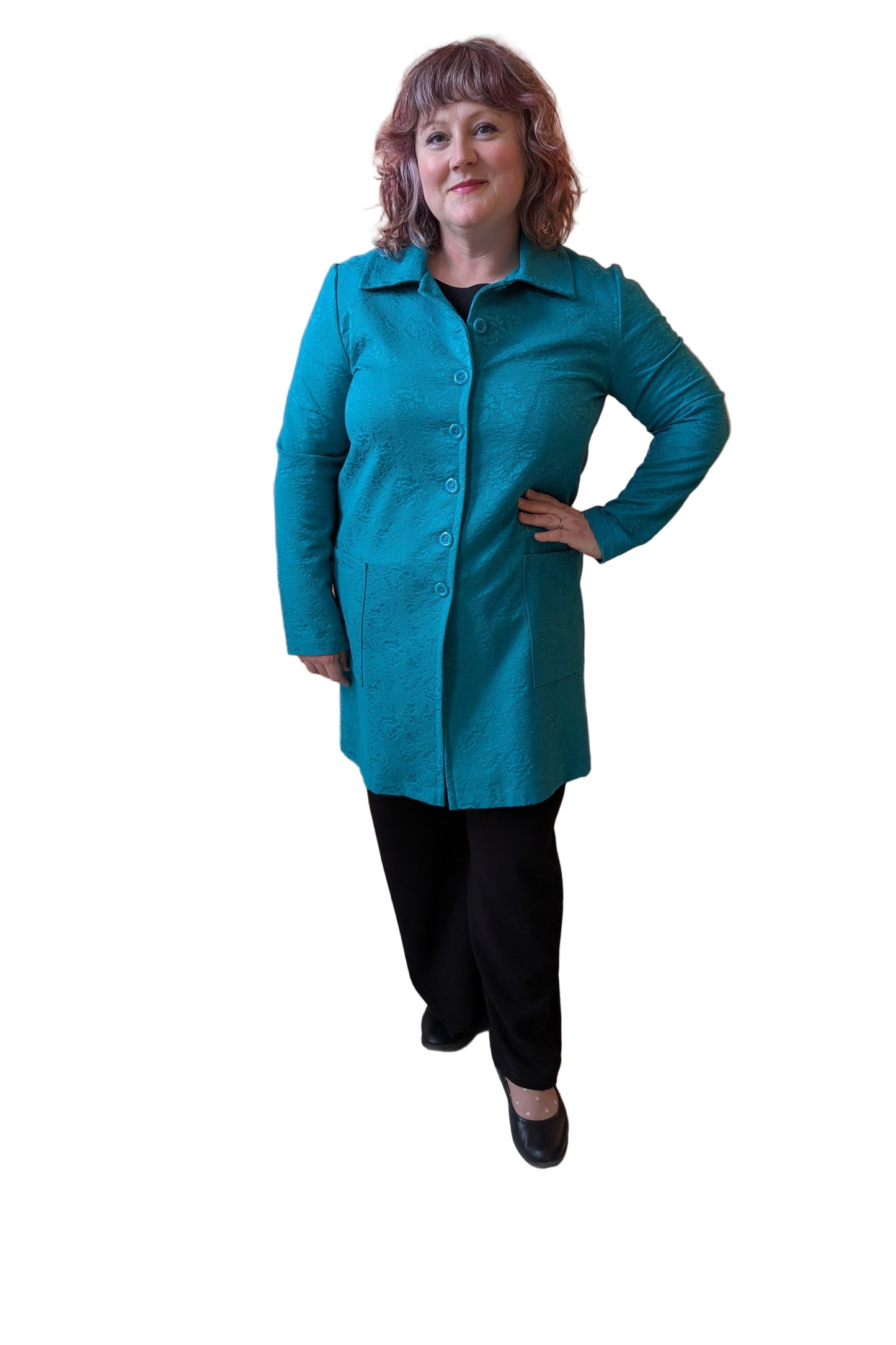 A woman wearing the Emmanuelle Coat by Kollontai in Turquoise jacquard with the Black pants. She is standing in front of a white background.
