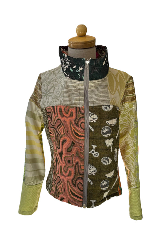 The Mosaique One of a Kind Reversible Jacket from Véronique d’Aragon is shown on a mannequin in front of a white background. This one of a kind piece features a patchwork of fabrics in green and earth tones, with a high collar, a zip front, and a cropped length.