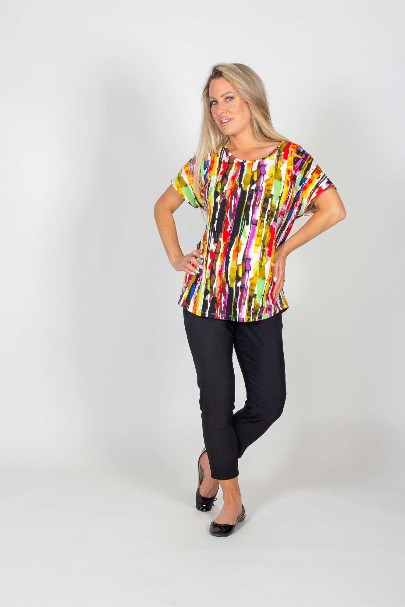 A woman wearing the Caroline Pant by Pure Essence in Black and a multicoloured top standing in front of a white background