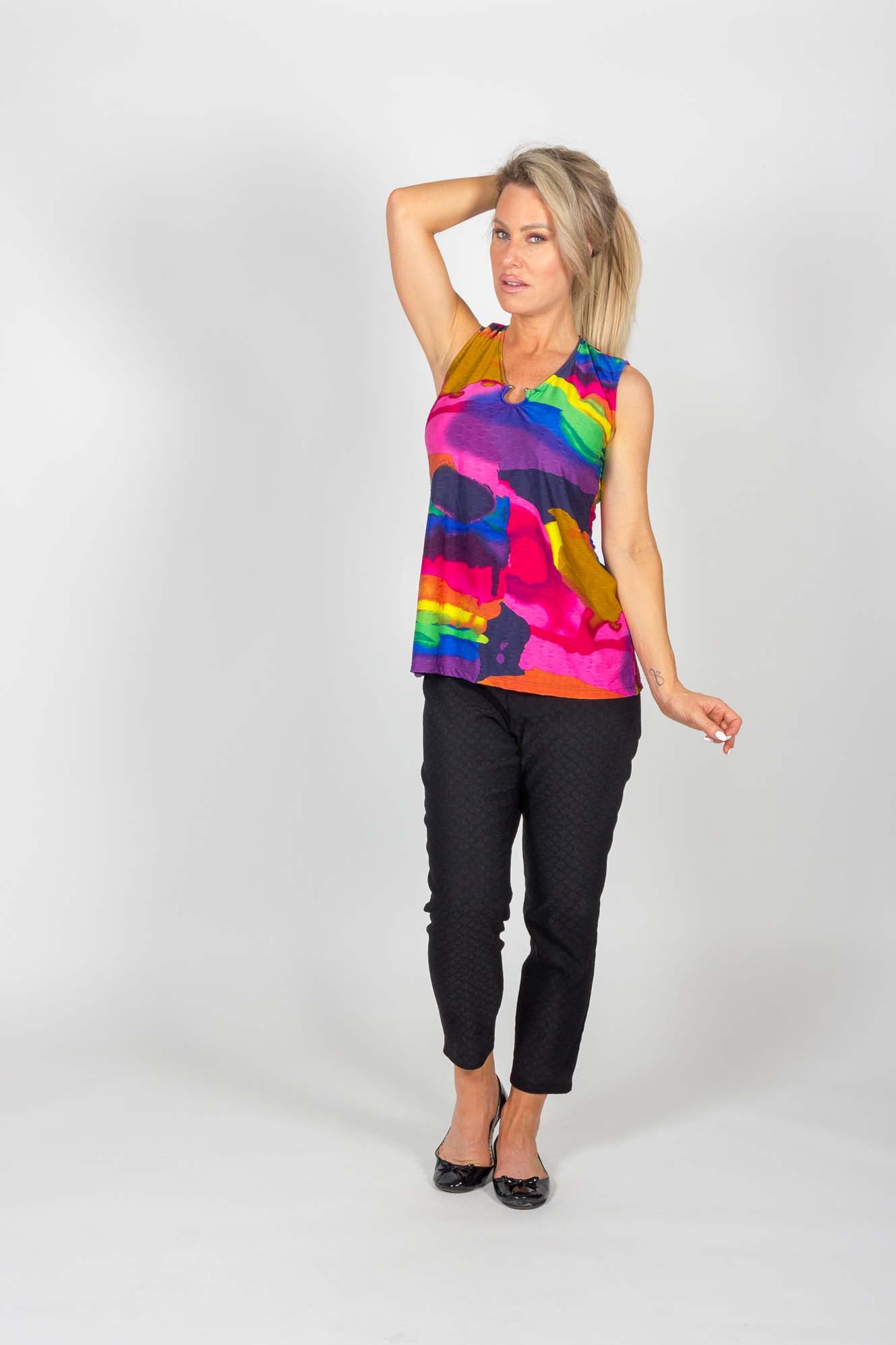 A woman wearing the Caroline Pant by Pure Essence in Black and a vibrant top standing in front of a white background