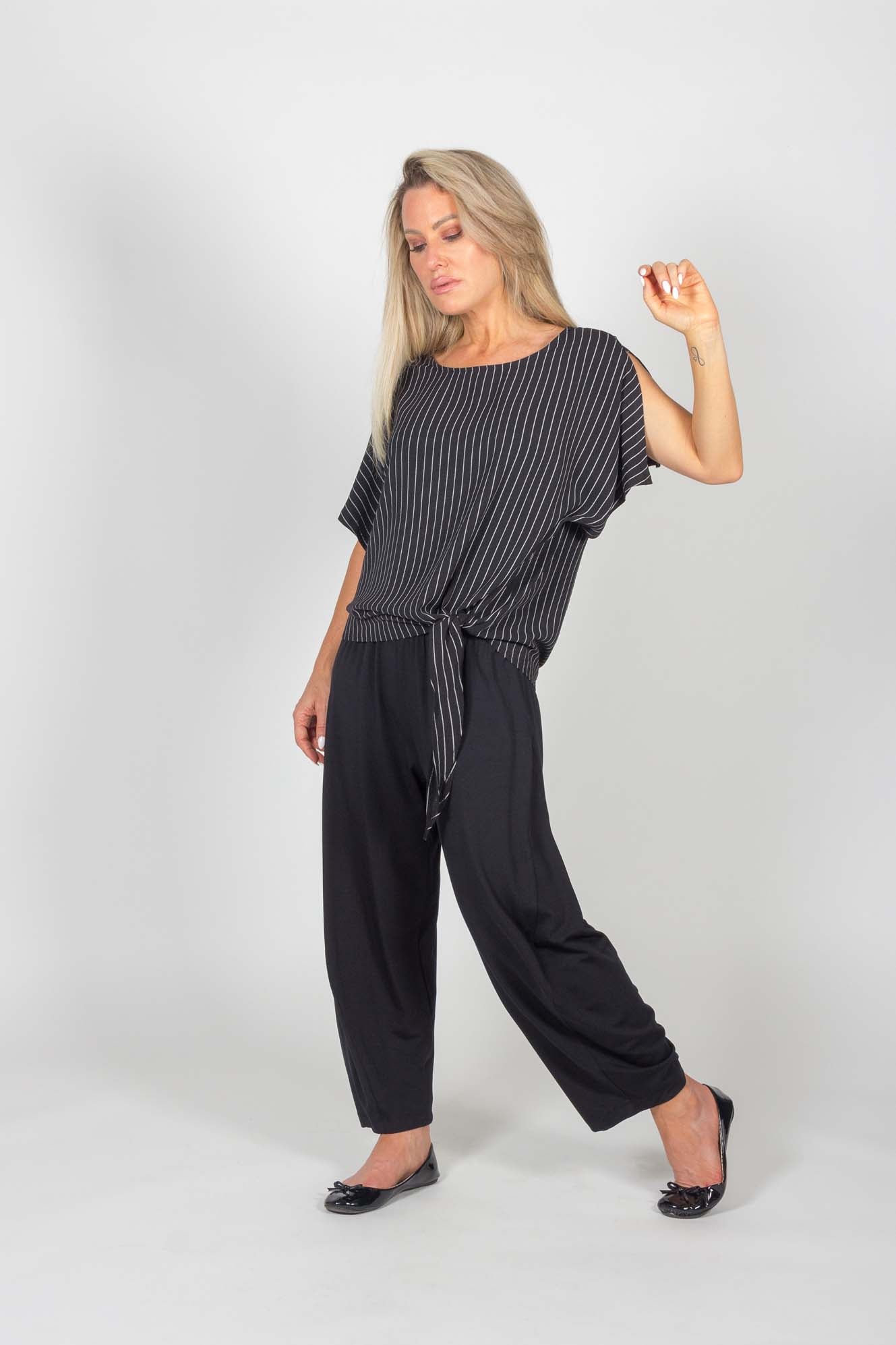 A woman wearing the Claire Top and the Celeste Harem Capri by Pure Essence in Black, standing in front of a white background