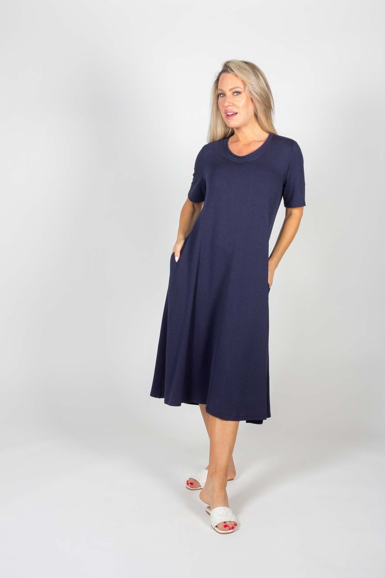 The Chloe Dress by Pure Essence in Navy is shown on a woman standing in front of a white background