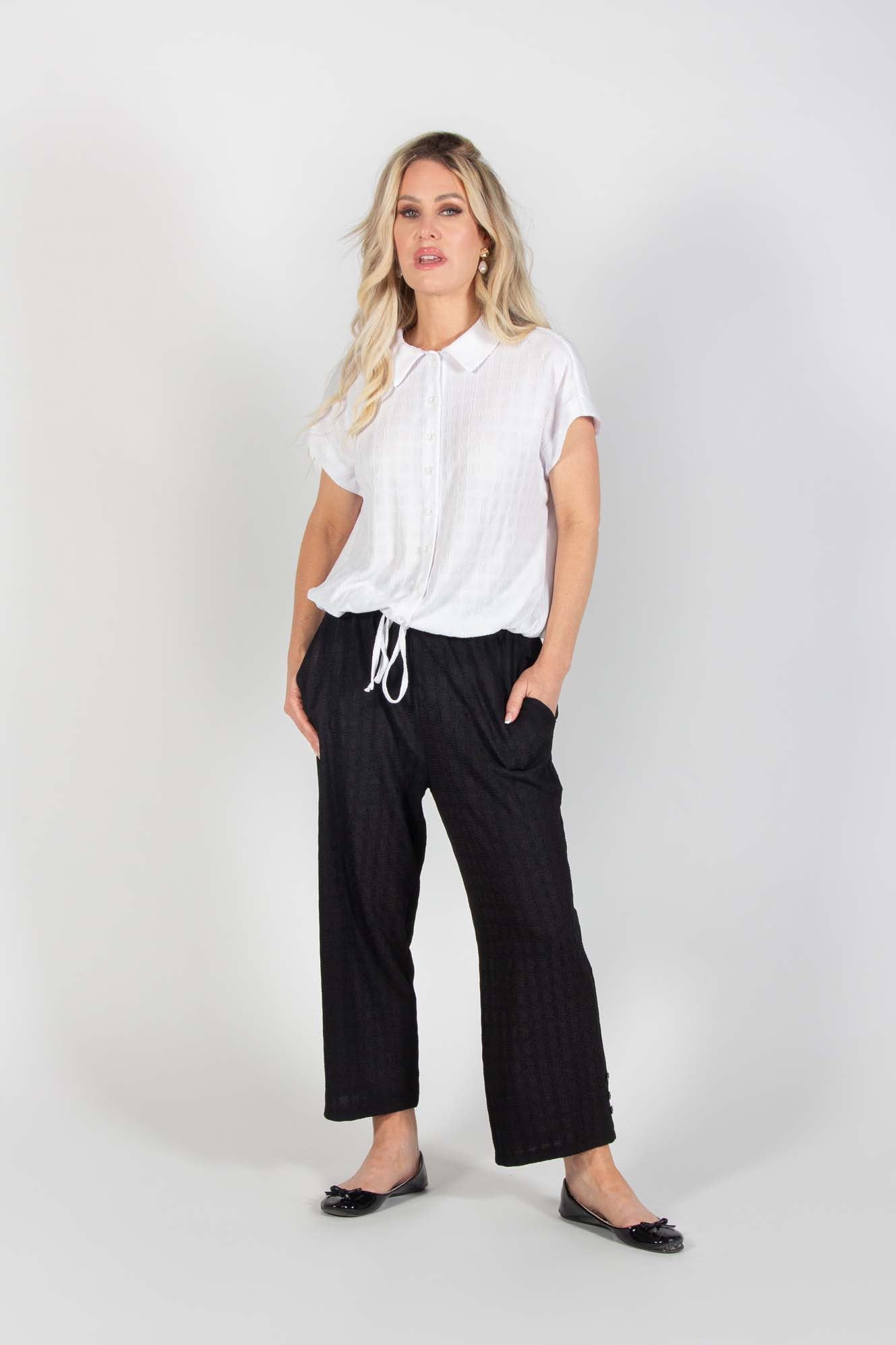 A woman wearing the Ciara Capri by Pure Essence in Black with the Candella Shirt in White stands in front of a white background
