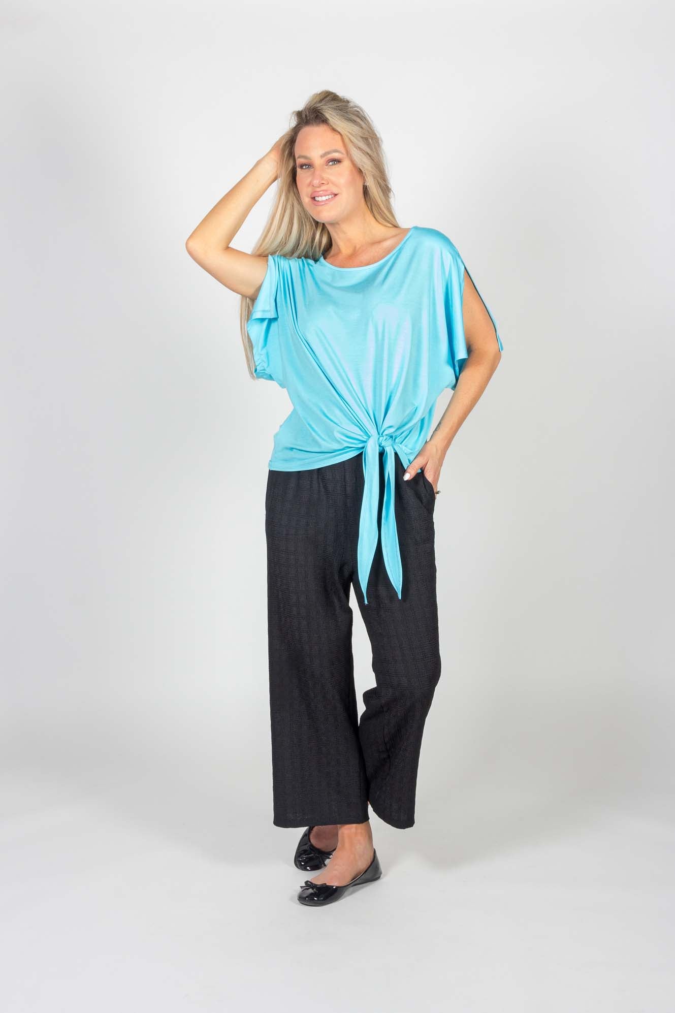 A woman wearing the Ciara Capri by Pure Essence in Black with a blue top stands in front of a white background
