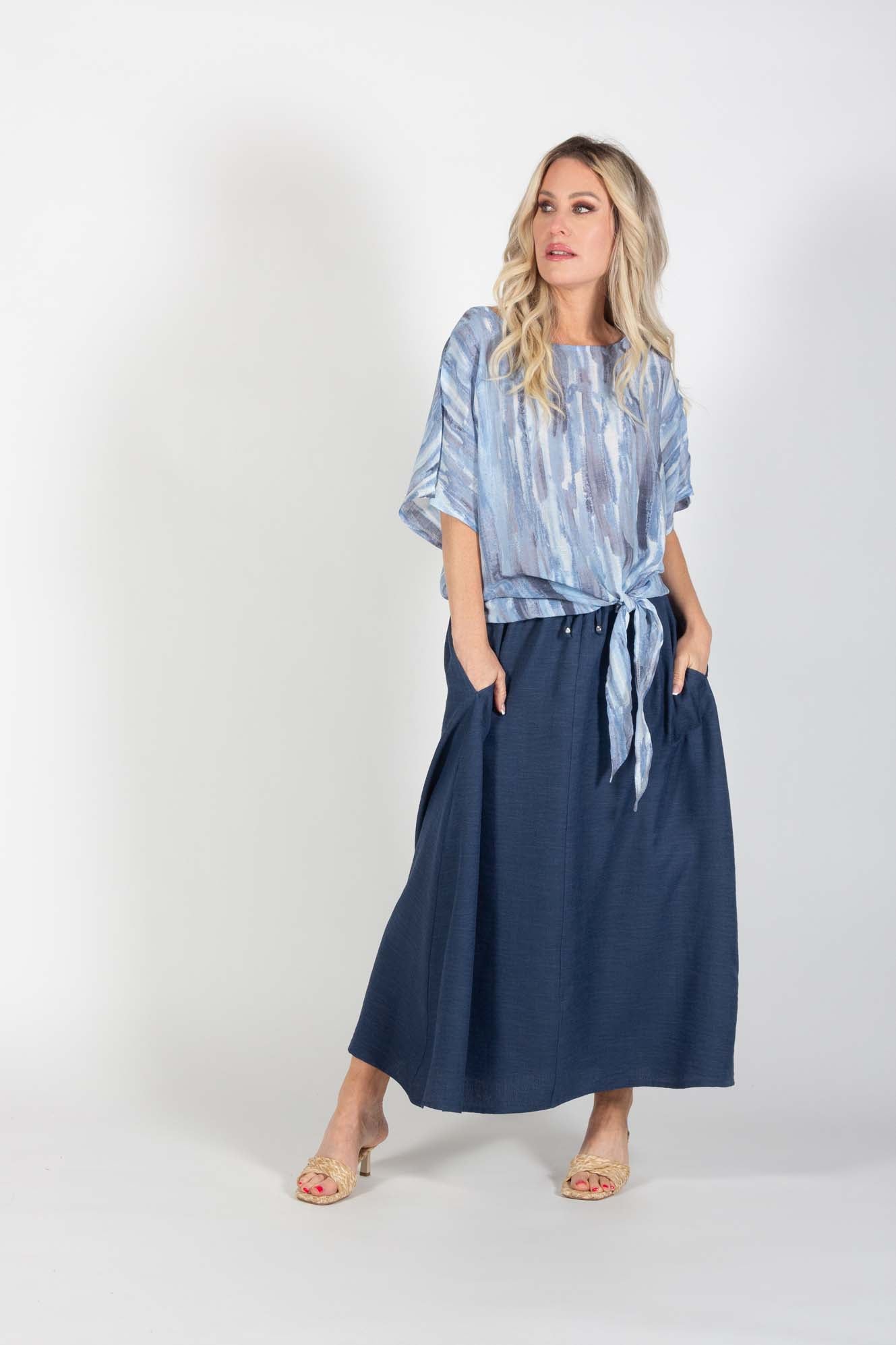 A woman wearing the Cole Skirt by Pure Essence in Indigo and the Chanelle Top in Sky/Blue, standing in front of a white background
