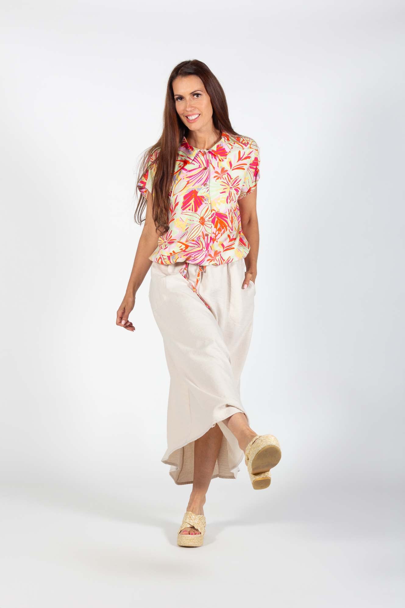 A woman wearing the Cole Skirt by Pure Essence in Sand with the Camilia Shirt, standing in front of a white background