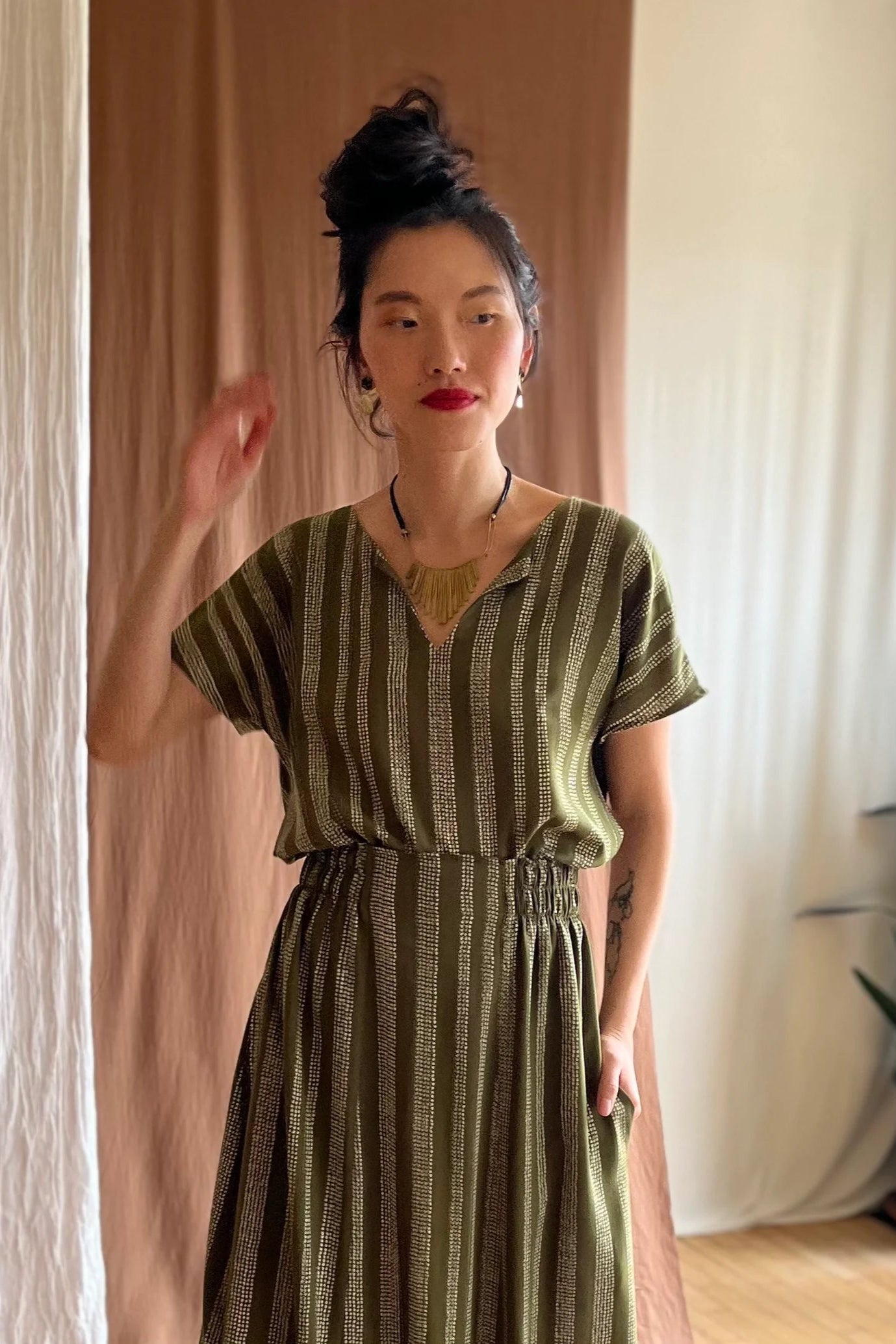 A woman wearing the Lucca Top by Kazak in Ivy Dots print, a short sleeved top with a notched V-neckline and a pleated yoke at the back. She is wearing it with a matching skirt and is standing in front of a beige curtain.
