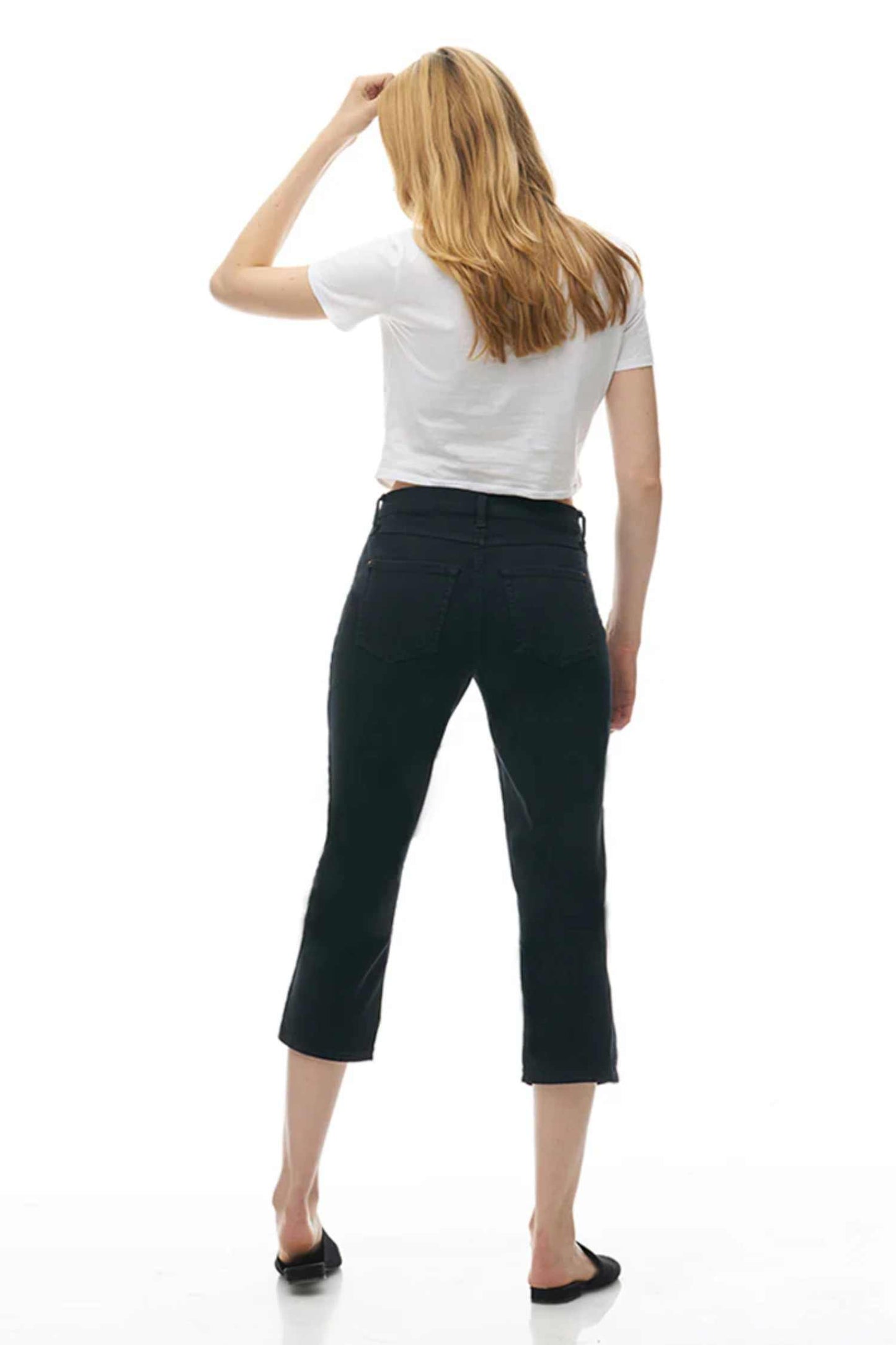 Back view of a woman wearing the CHLOE Classic Rise Straight Leg Capri Yoga Jeans in Black standing in front of a white background
