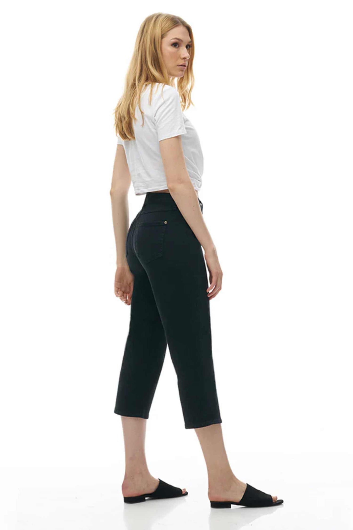 Side view of a woman wearing the CHLOE Classic Rise Straight Leg Capri Yoga Jeans in Black standing in front of a white background