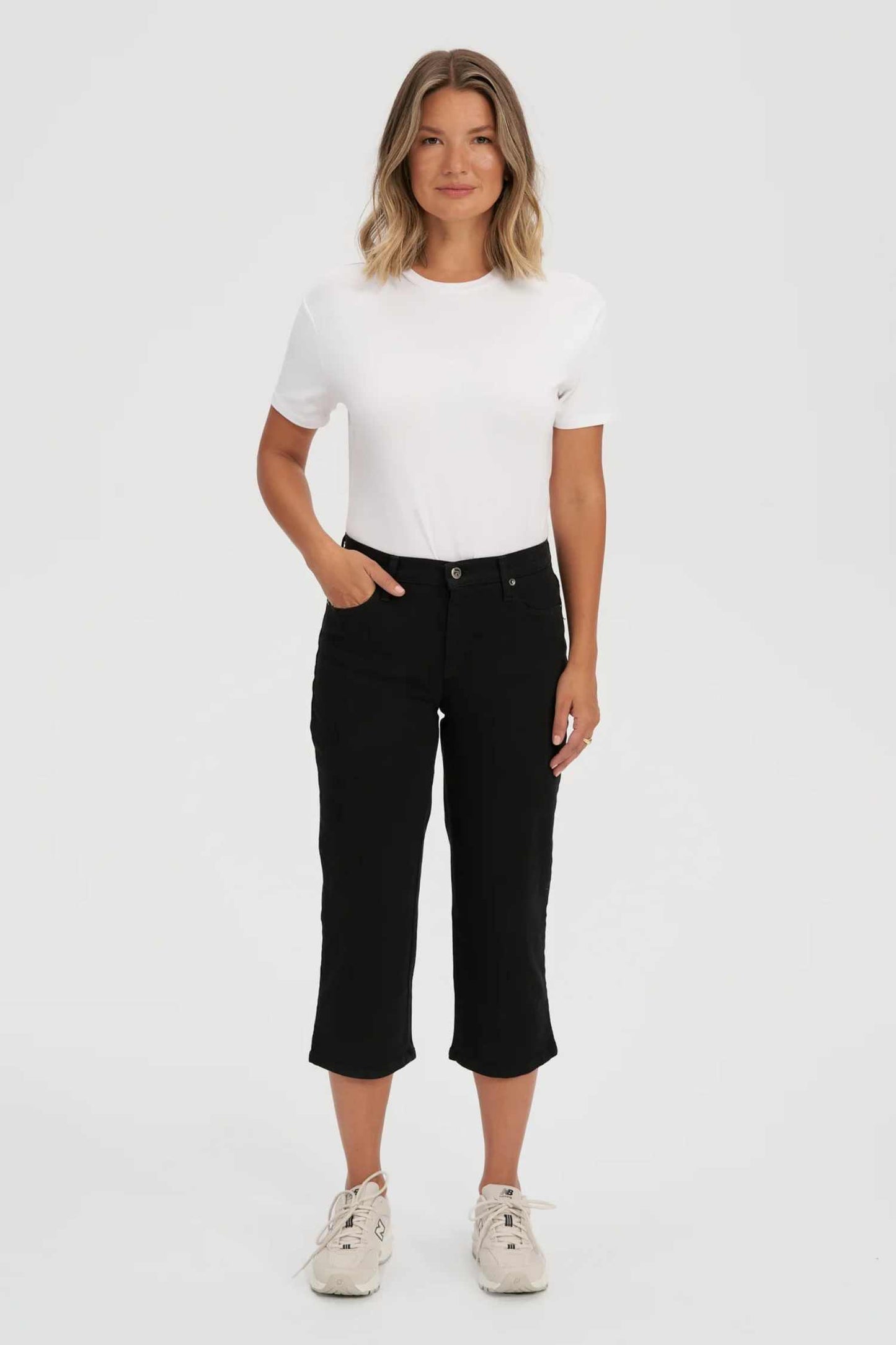 Woman wearing the CHLOE Classic Rise Straight Leg Capri Yoga Jeans in Black standing in front of a white background