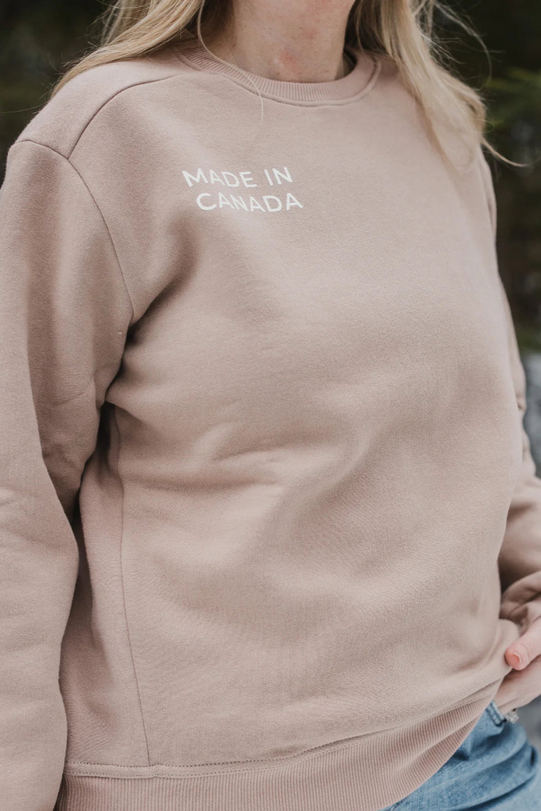 Close up neck-down view of a woman wearing the Made in Canada Unisex Crewneck Sweatshirt by Blondie in Stucco.