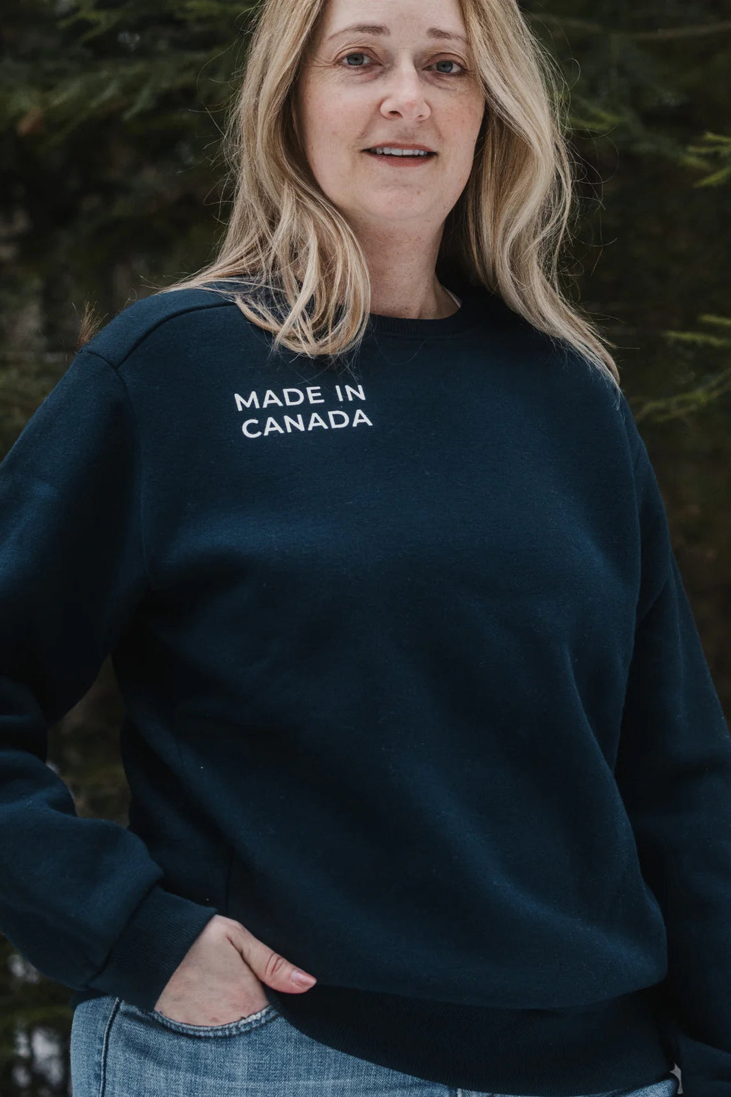 Waist-up view of a woman wearing the Made in Canada Unisex Crewneck Sweatshirt by Blondie in Navy. She is standing outside.