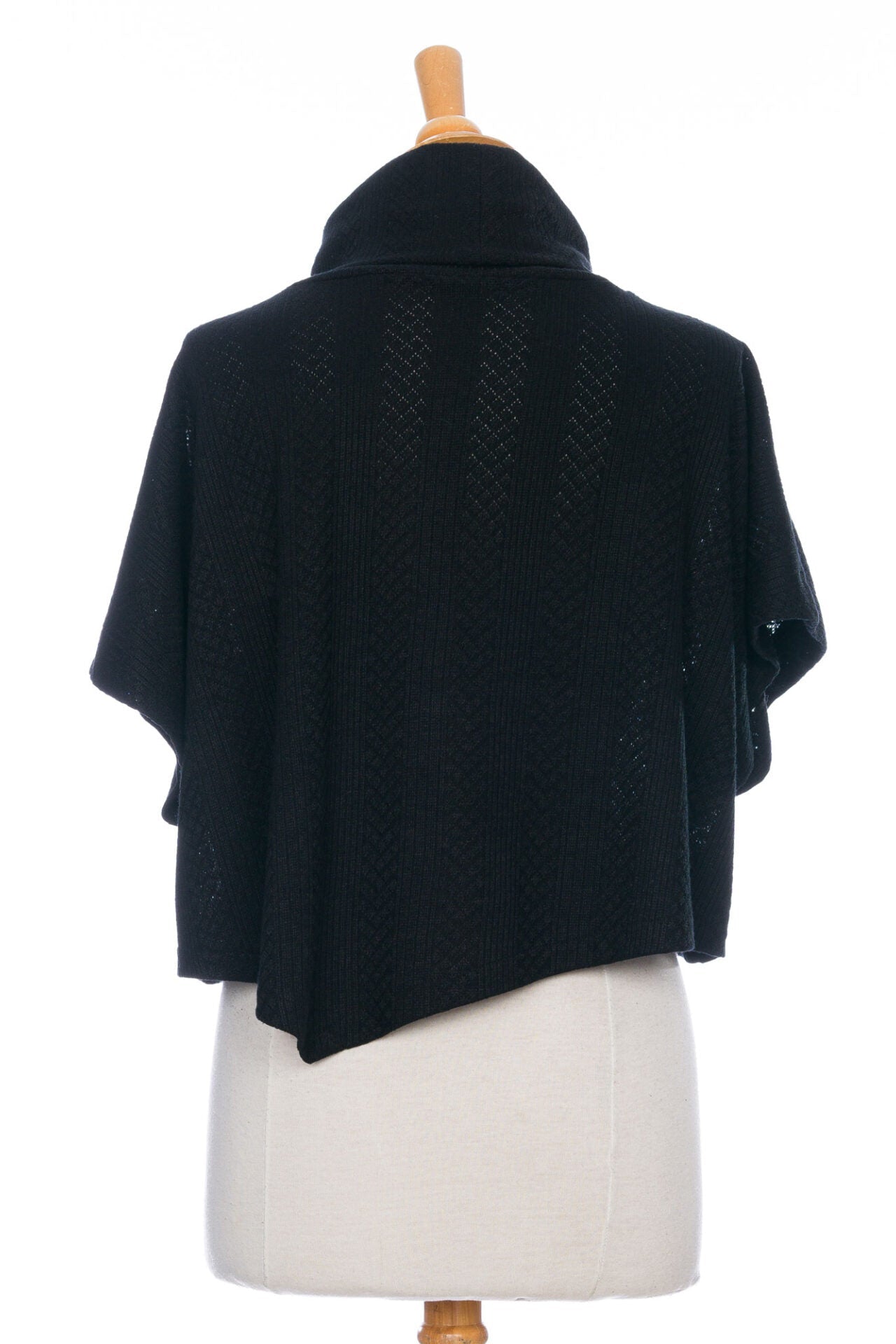 A back view of the Lupin Poncho-Bolero in Ivory by Rien ne se Perd, featuring soft jacquard knit, a loose turtleneck, and an asymmetrical hem, is shown on a mannequin in front of a white background.