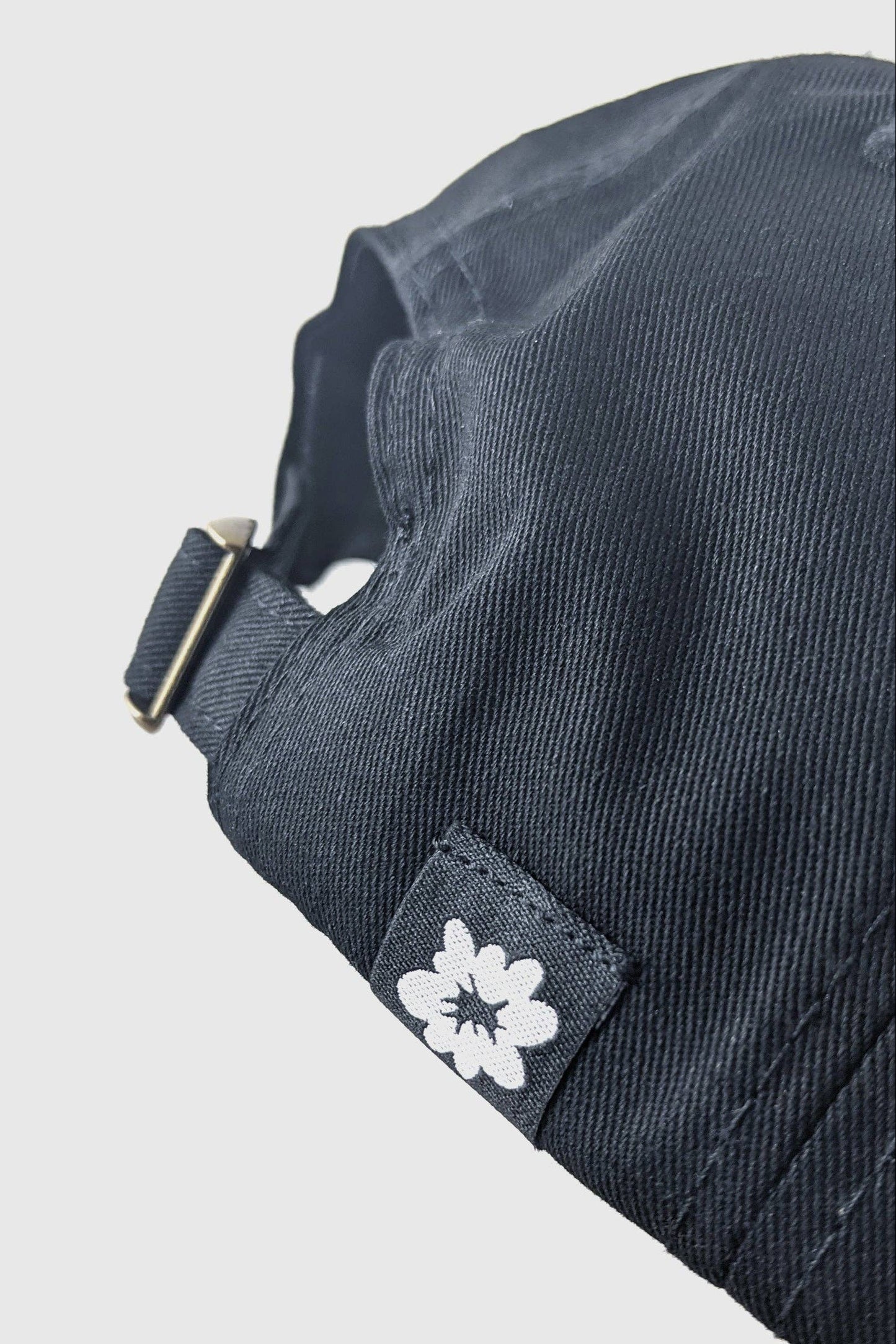 Close up of the back of the Split Hat from Badaboöm Studio, featuring an embroidered split view of a woman's face in white on a black background, shown against a light grey background.
