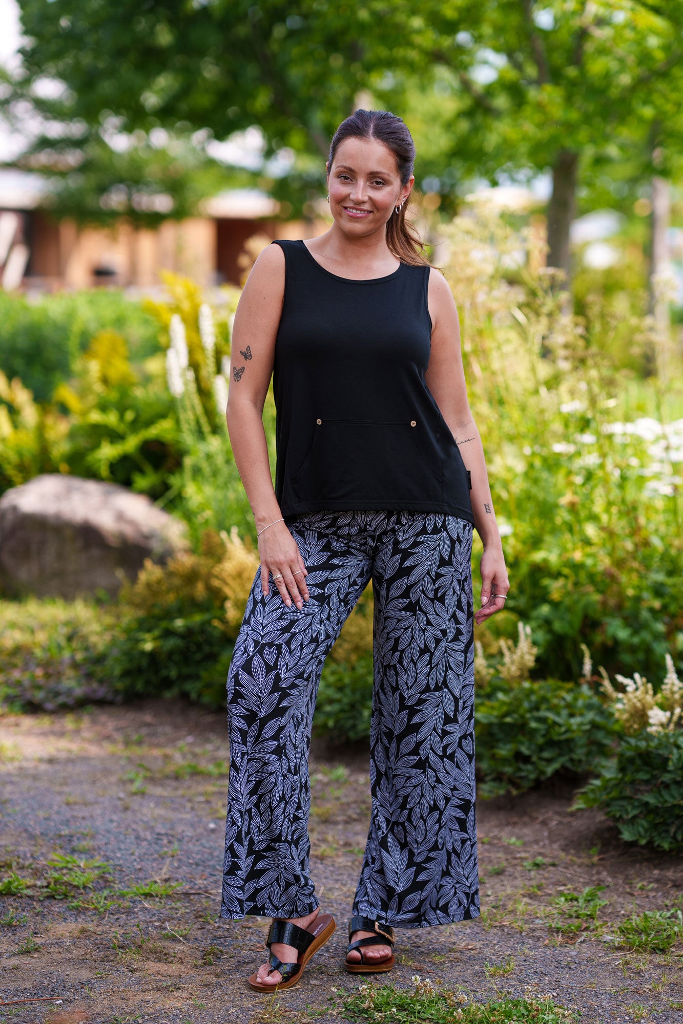 A woman wearing the Rumba Palazzo Pants by Rien ne se Perd in Black and White Foliage with a black tank, standing outside.