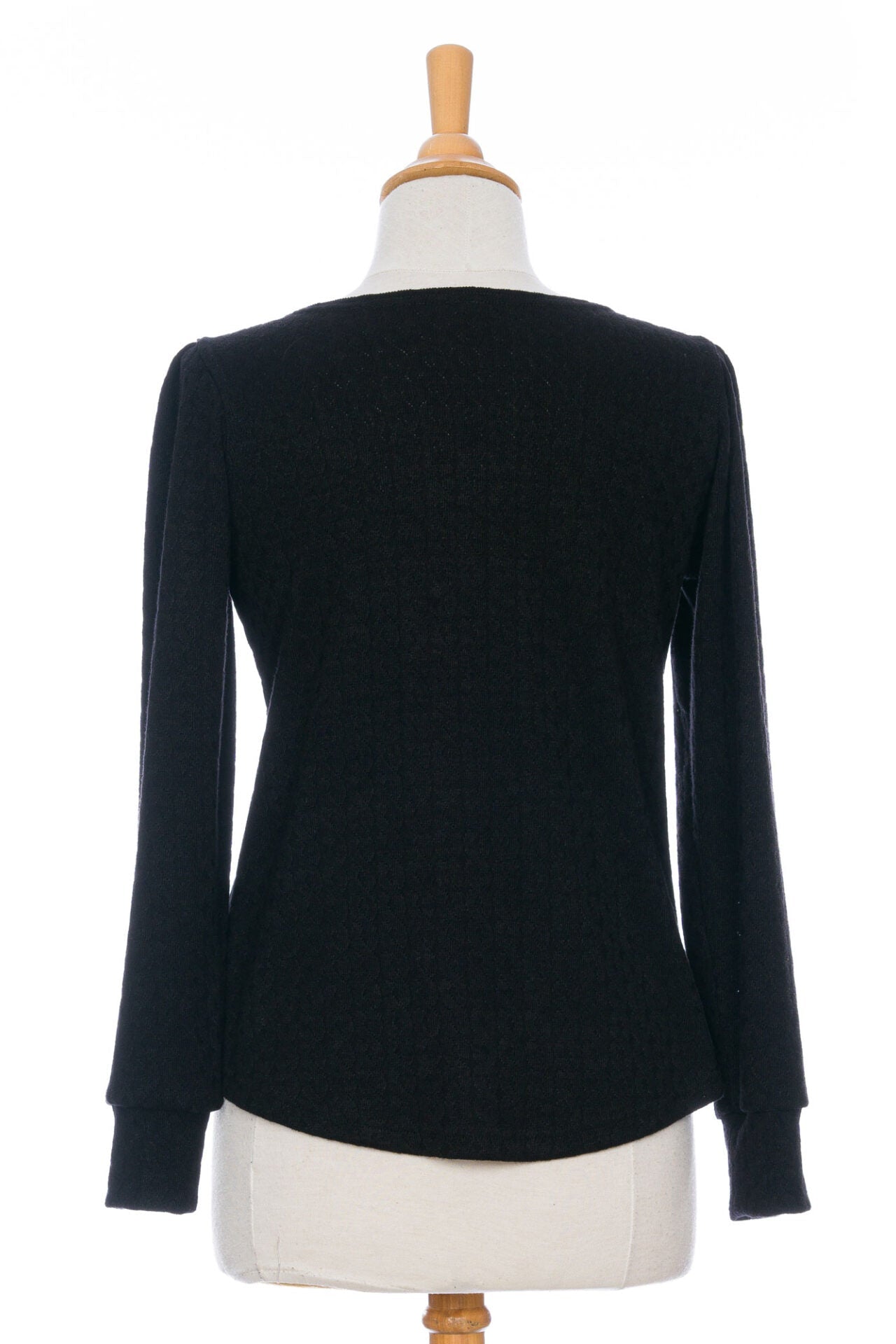 Back view of the Camarine Sweater by Rien ne se Perd in Black, a cable knit sweater with a scooped neck, puffed shoulders, and gathered cuffs, shown on a mannequin agains a white background.
