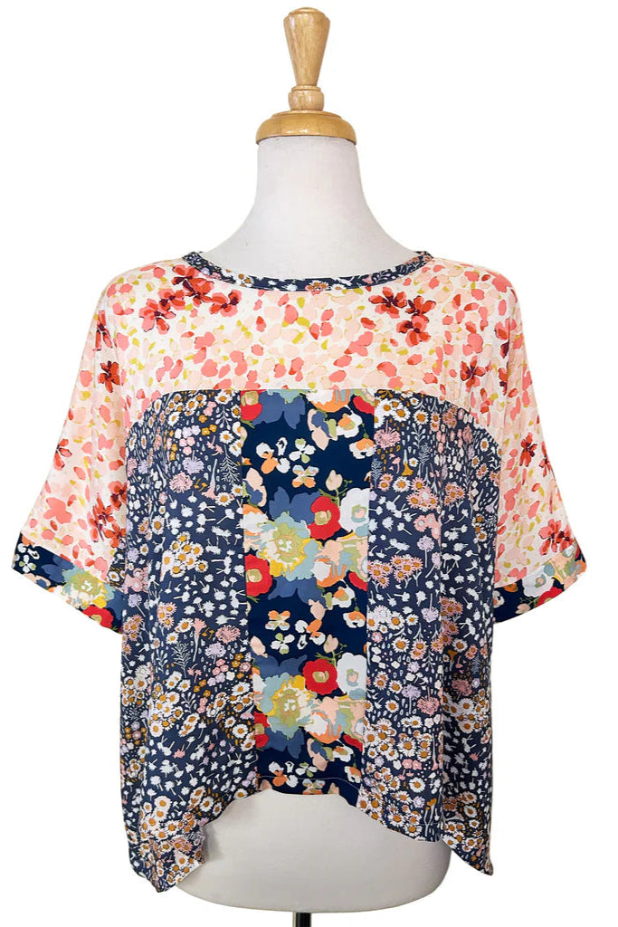 The Chloe Top by Desserts and Skirts in Floral Strip, featuring a round neck, batwing sleeves, and a loose and flowing fit, is shown on a mannequin in front of a white background.