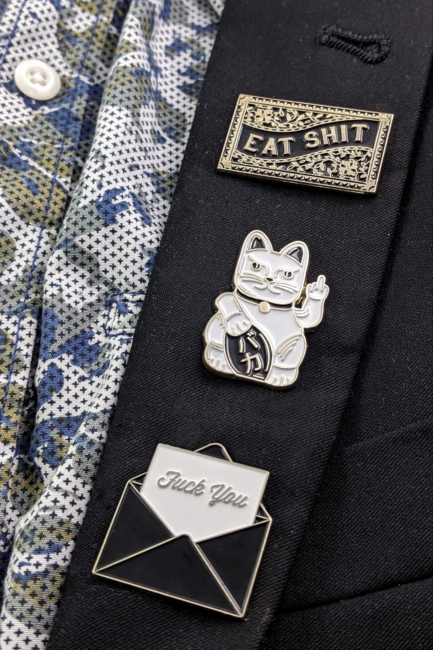 The Fuck You Pin by Badaboöm Studio is shown along with other sassy pins on a black suit lapel.