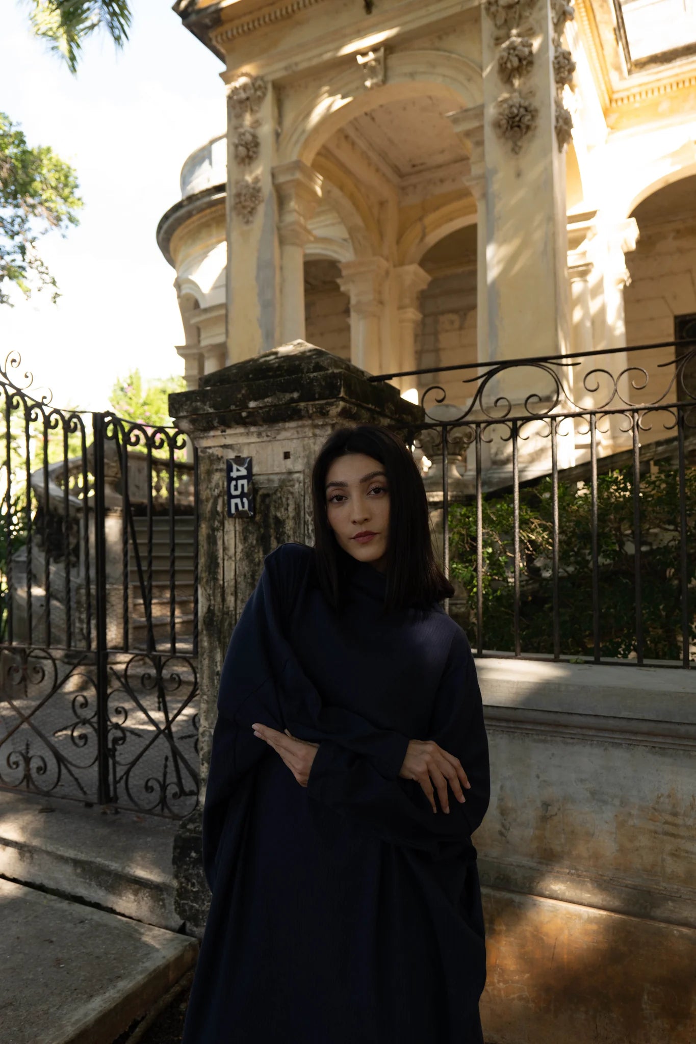 Back view of a woman wearing the Frankfurt Dress by MAS in Blueberry, a One Size ribbed cotton dress with a mock turtleneck, long batwing sleeves, and midi length. She is standing outside a historic building.