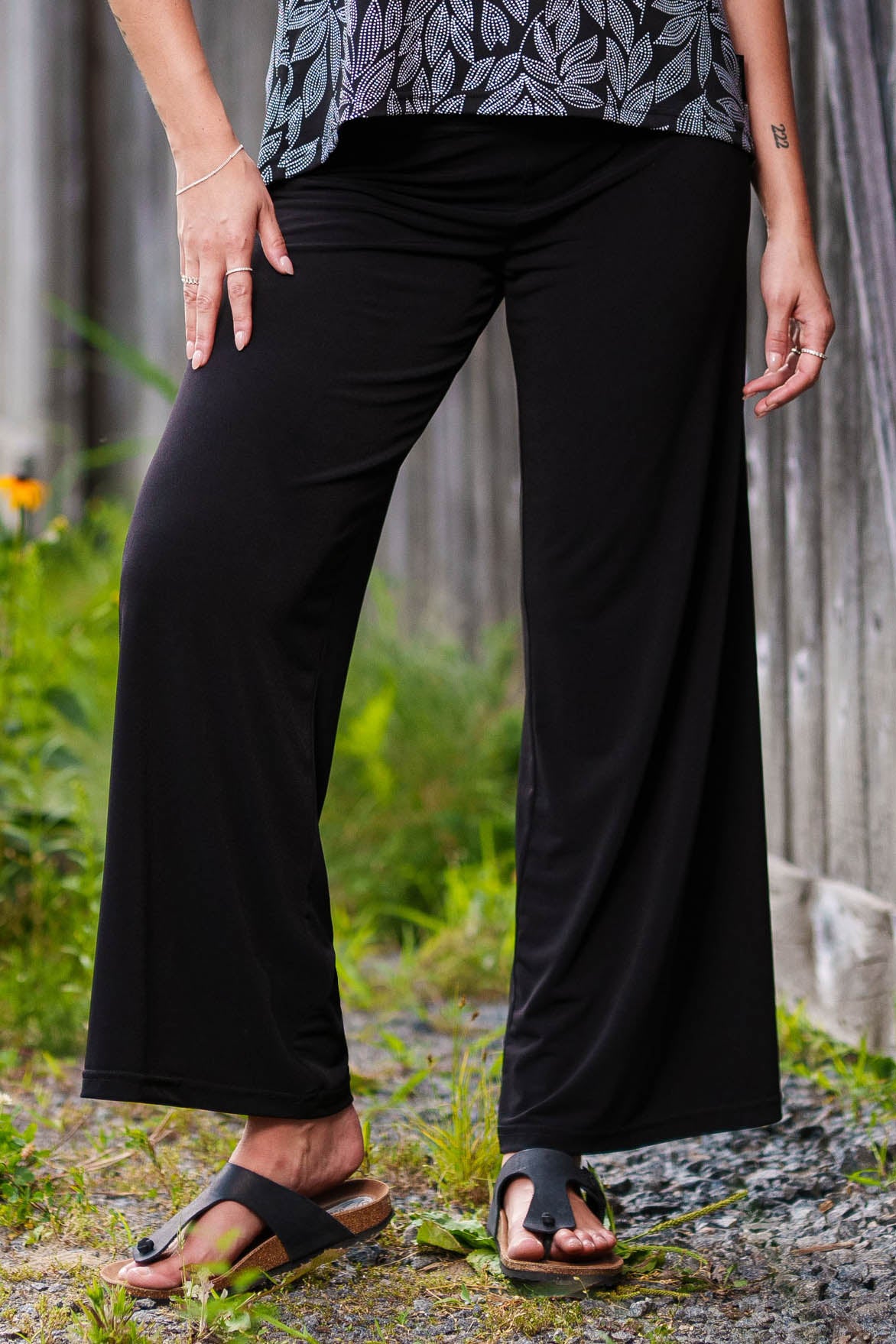 A waist-down view of a woman wearing the Rien ne se Perd Rumba Palazzo Pants in Black and the Swing Cami in Black and White Foliage.
