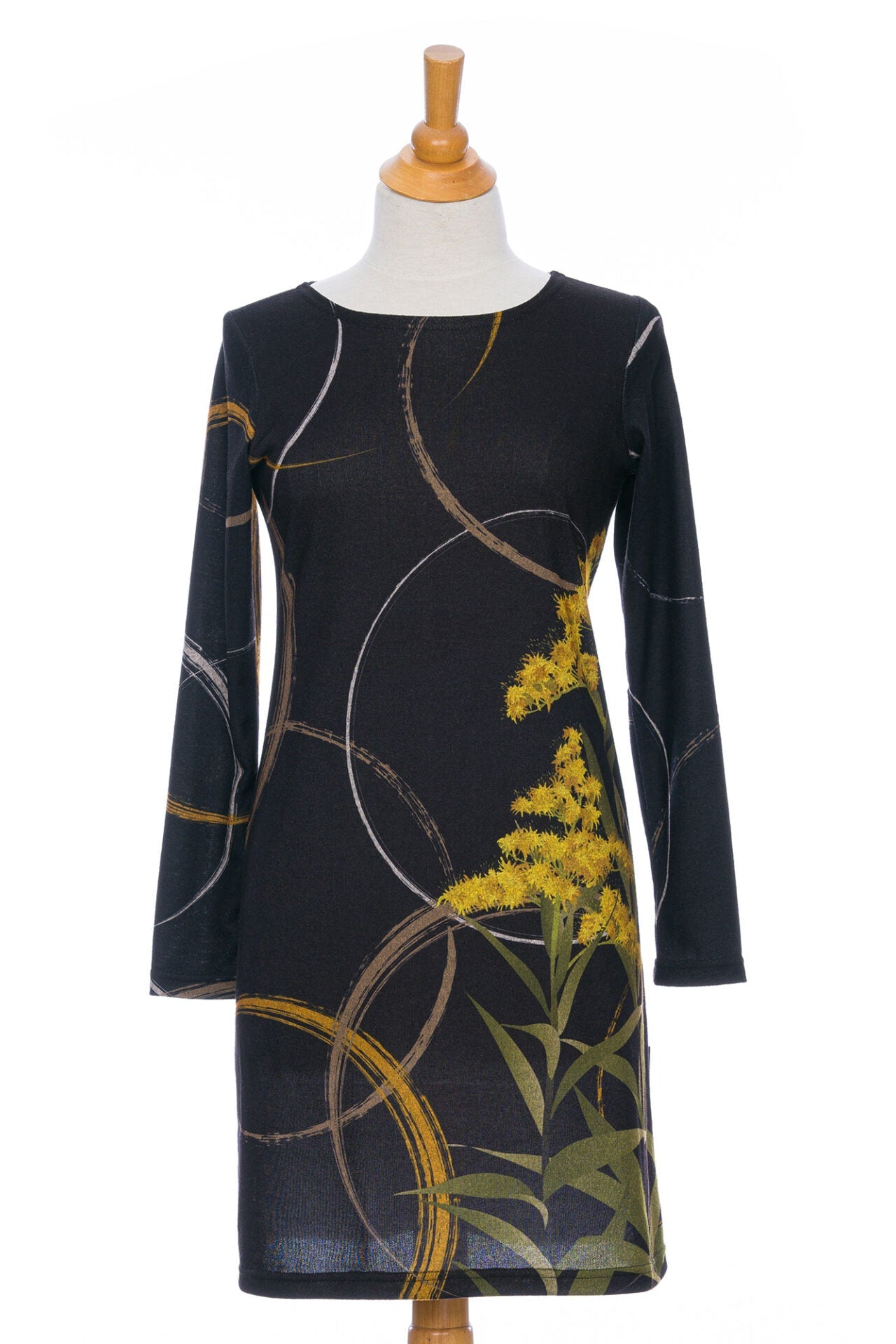 The Flore Dress by Rien ne se Perd in Bordure, a semi-fitted black dress with a flora inspired print, long sleeves, a round neck, and hem that hits above the knees, is shown on a mannequin in front of a white background.